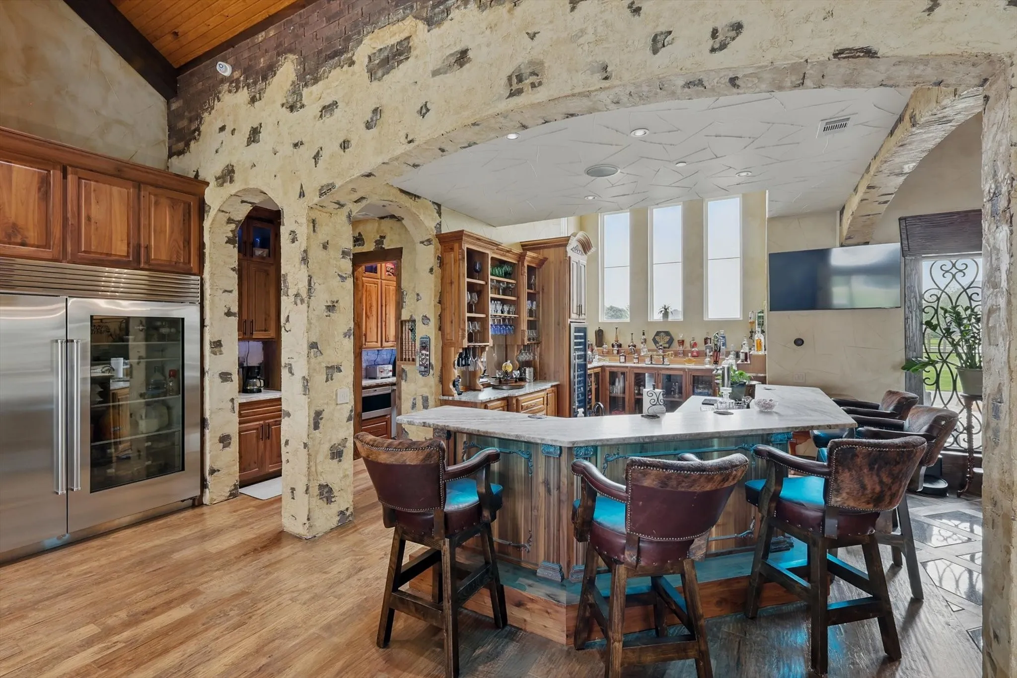 Kitchen with arched walkways, a breakfast bar area, wallpapered walls, wood finish cabinetry, and stainless steel built in fridge