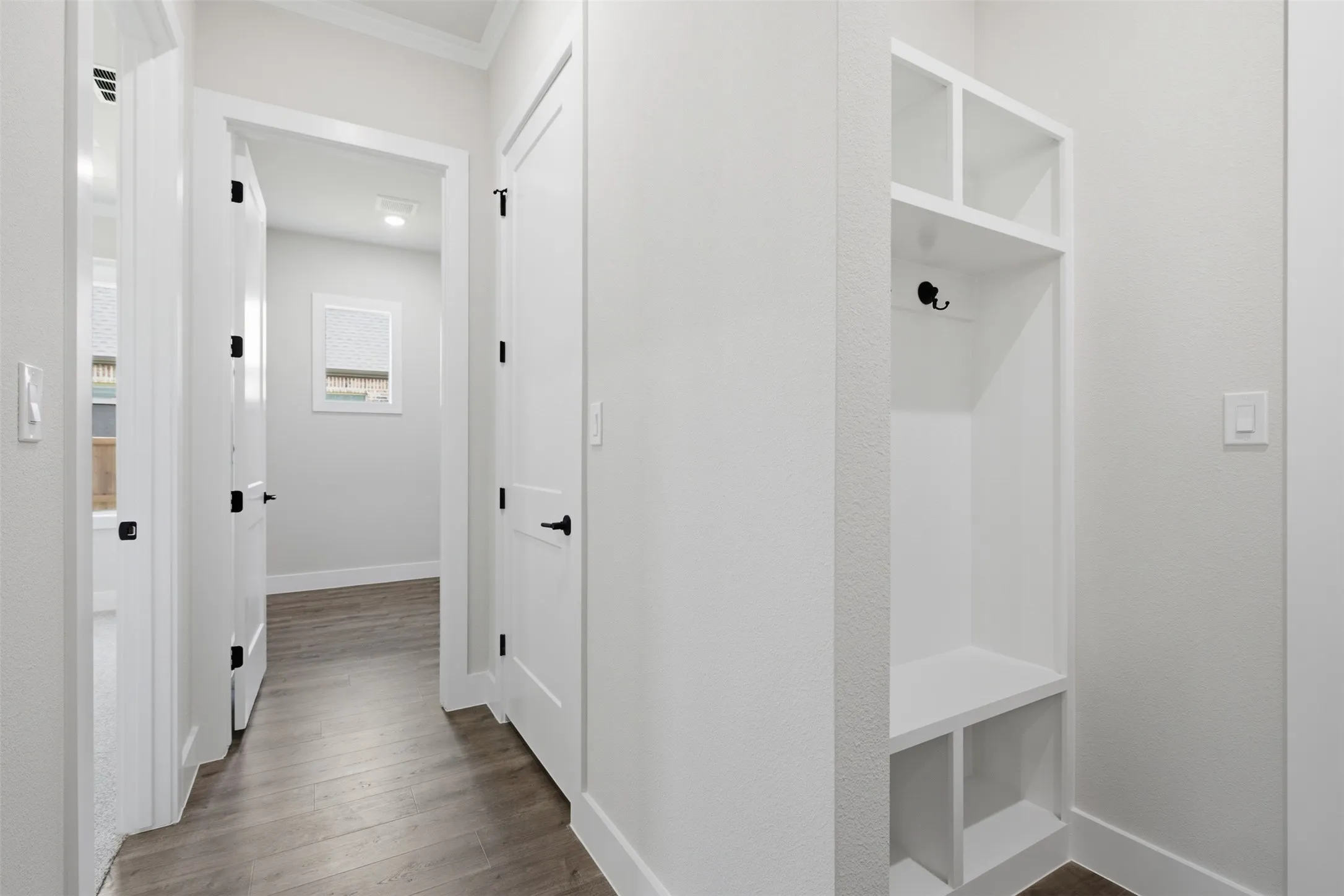 Hallway featuring wood-finish flooring and multiple white paneled doors with matte black hardware