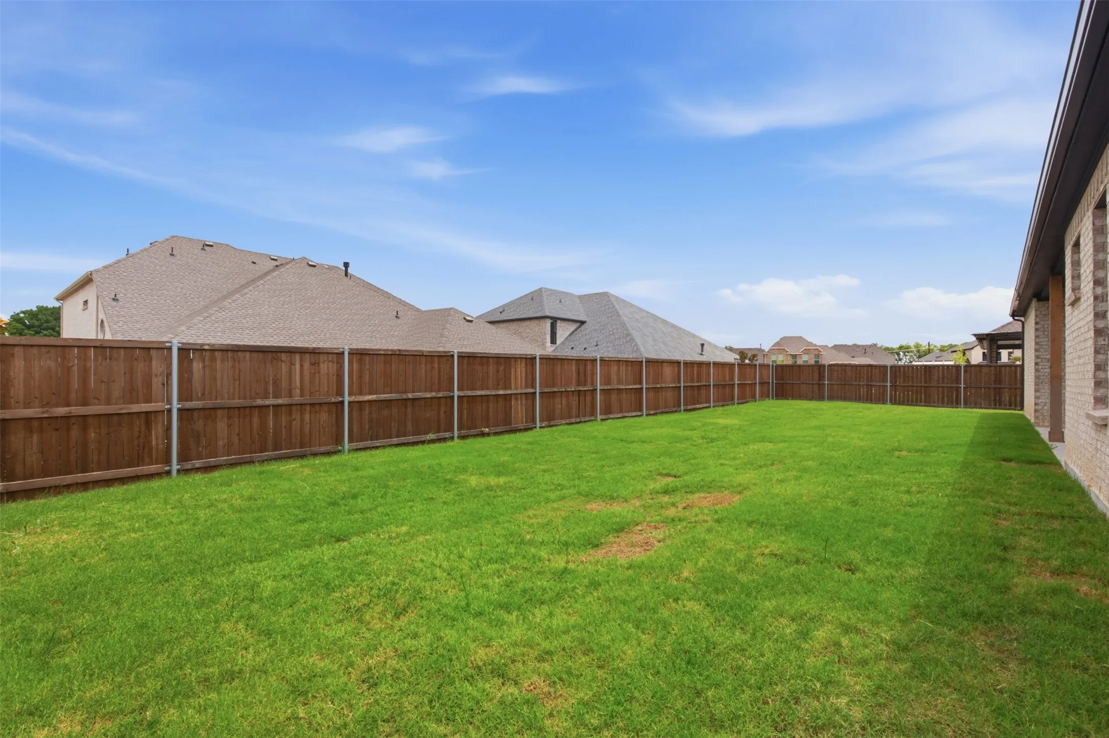 Expansive backyard featuring a lush green lawn, full privacy fencing, and brick exterior