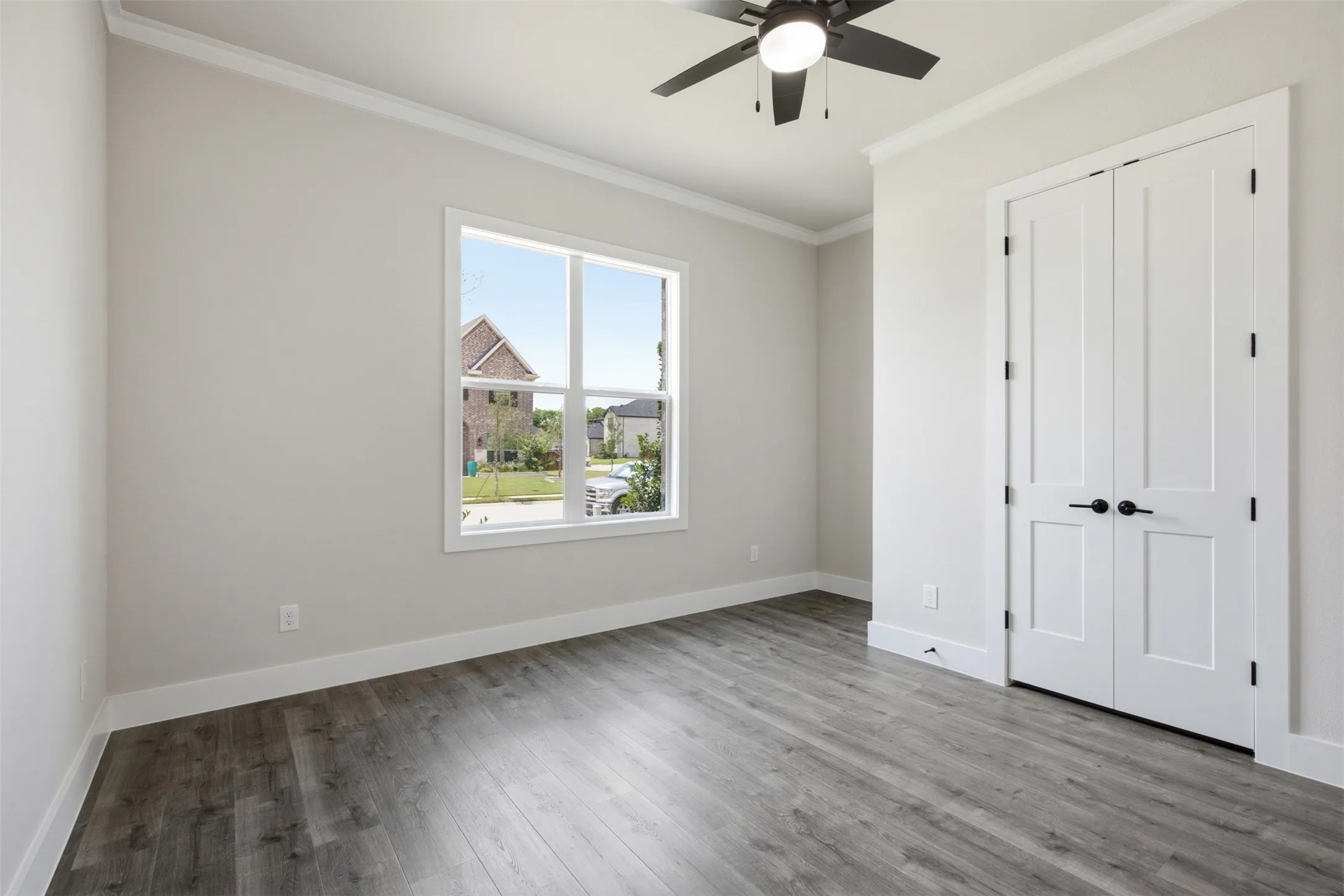Room featuring wood-finish flooring, a contemporary ceiling fan, and a double-door closet with matte black hardware