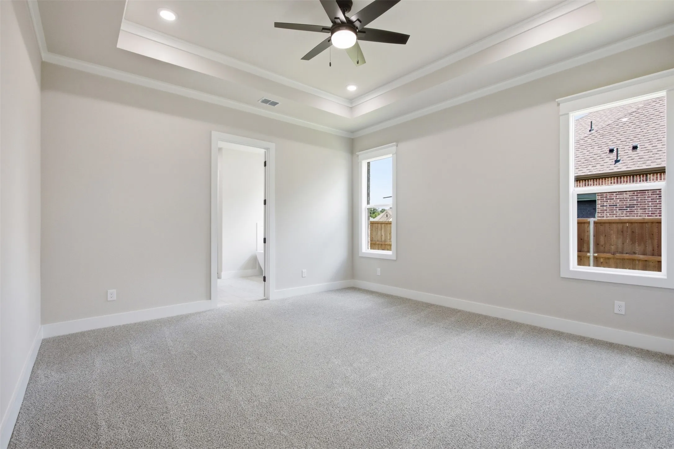 Spacious room featuring light-colored carpeting, a tray ceiling with recessed lighting, and a ceiling fan
