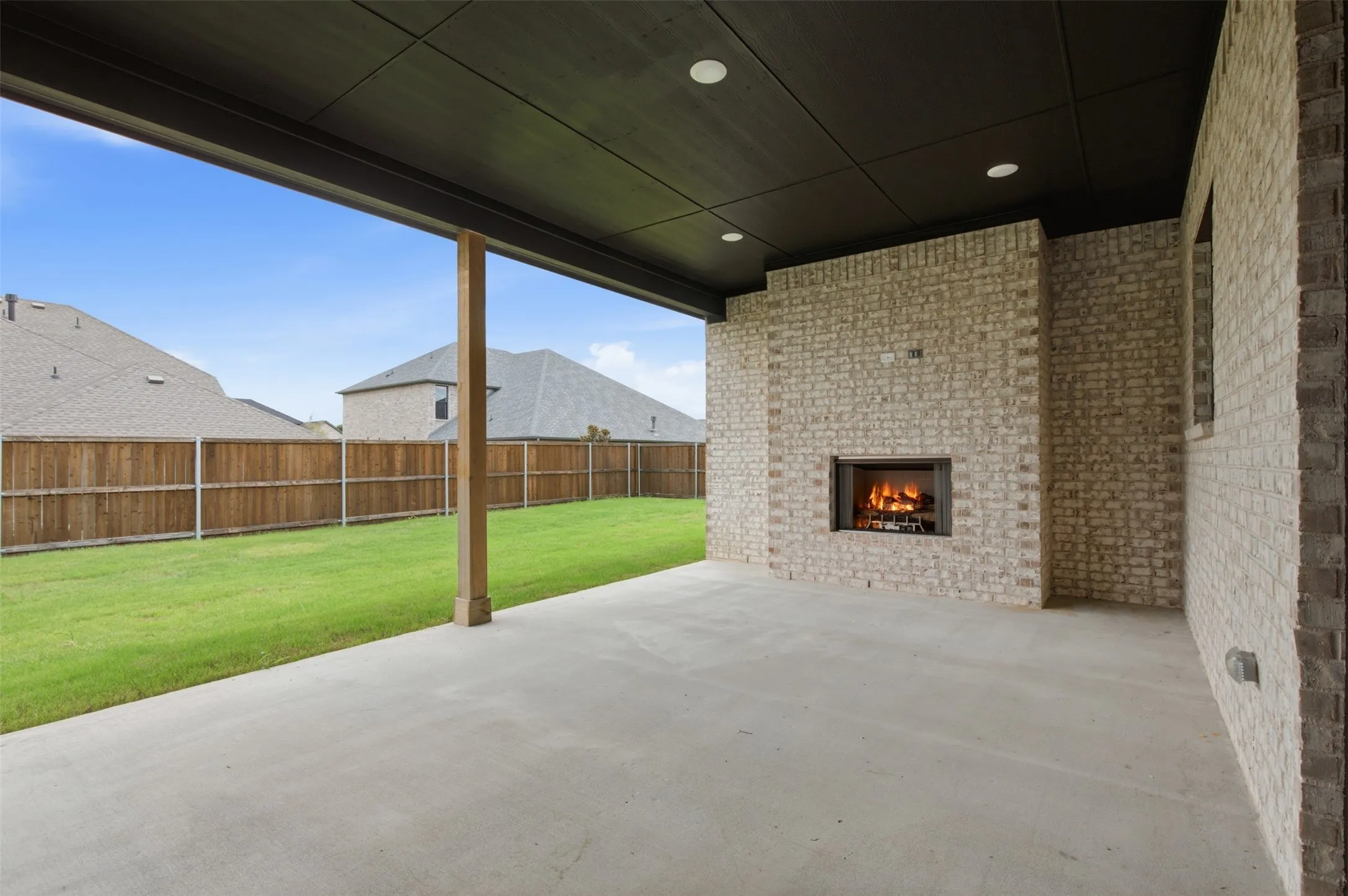 Covered patio featuring an outdoor fireplace with a dark metal surround, a concrete floor, and a dark paneled ceiling with recessed lighting