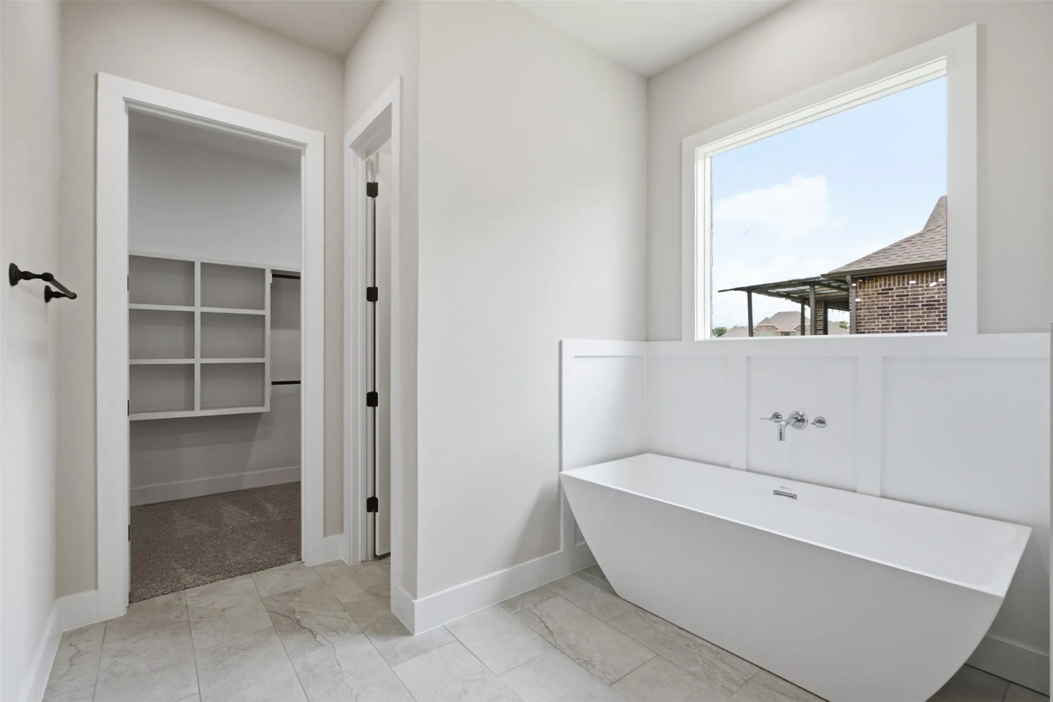 Bathroom featuring a freestanding tub with wall-mounted fixtures, tile flooring, and a window with white trim