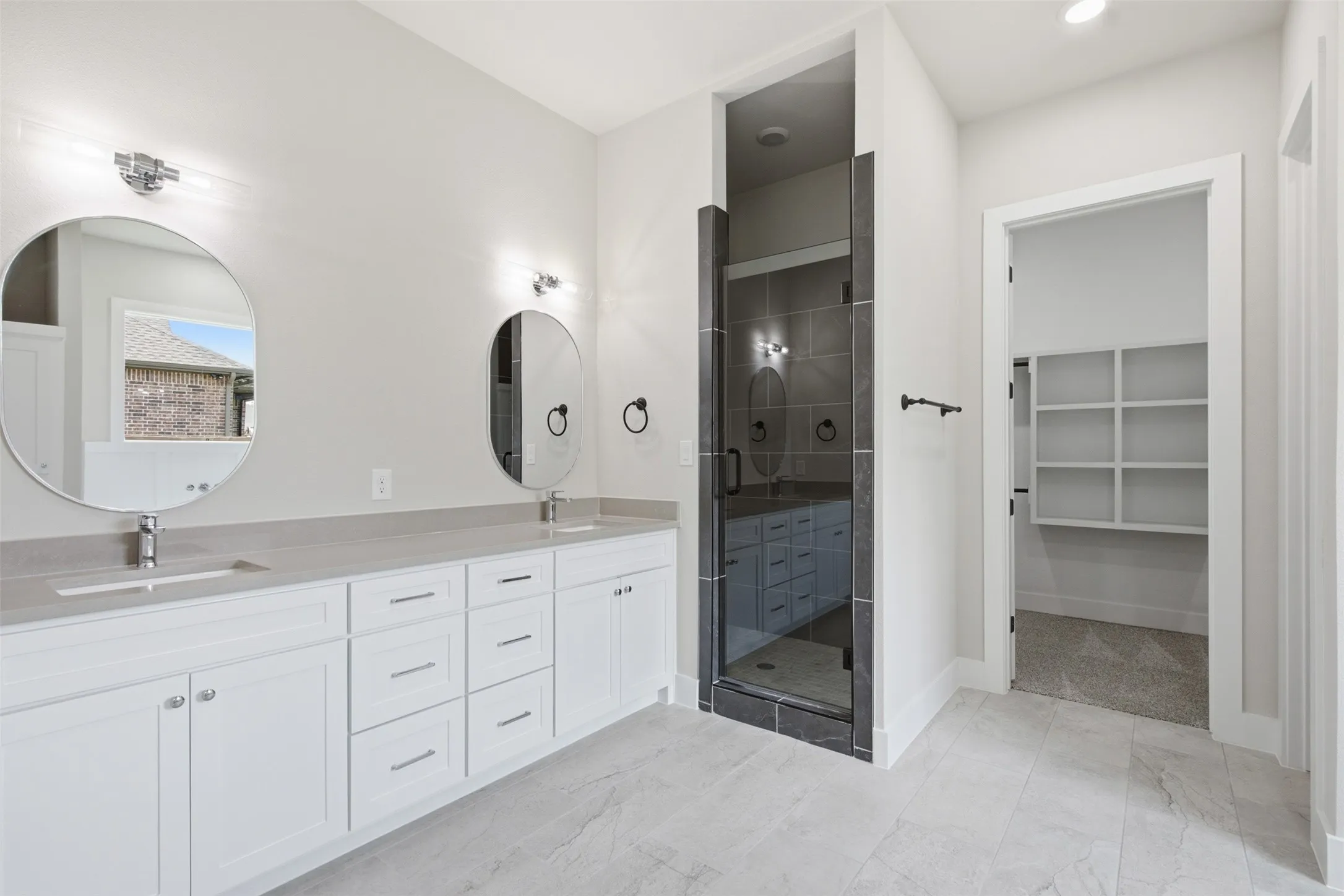 Contemporary bathroom featuring a double vanity with stone countertops and undermount sinks, a glass-enclosed shower with tiled walls, and a separate walk-in closet with built-in shelving