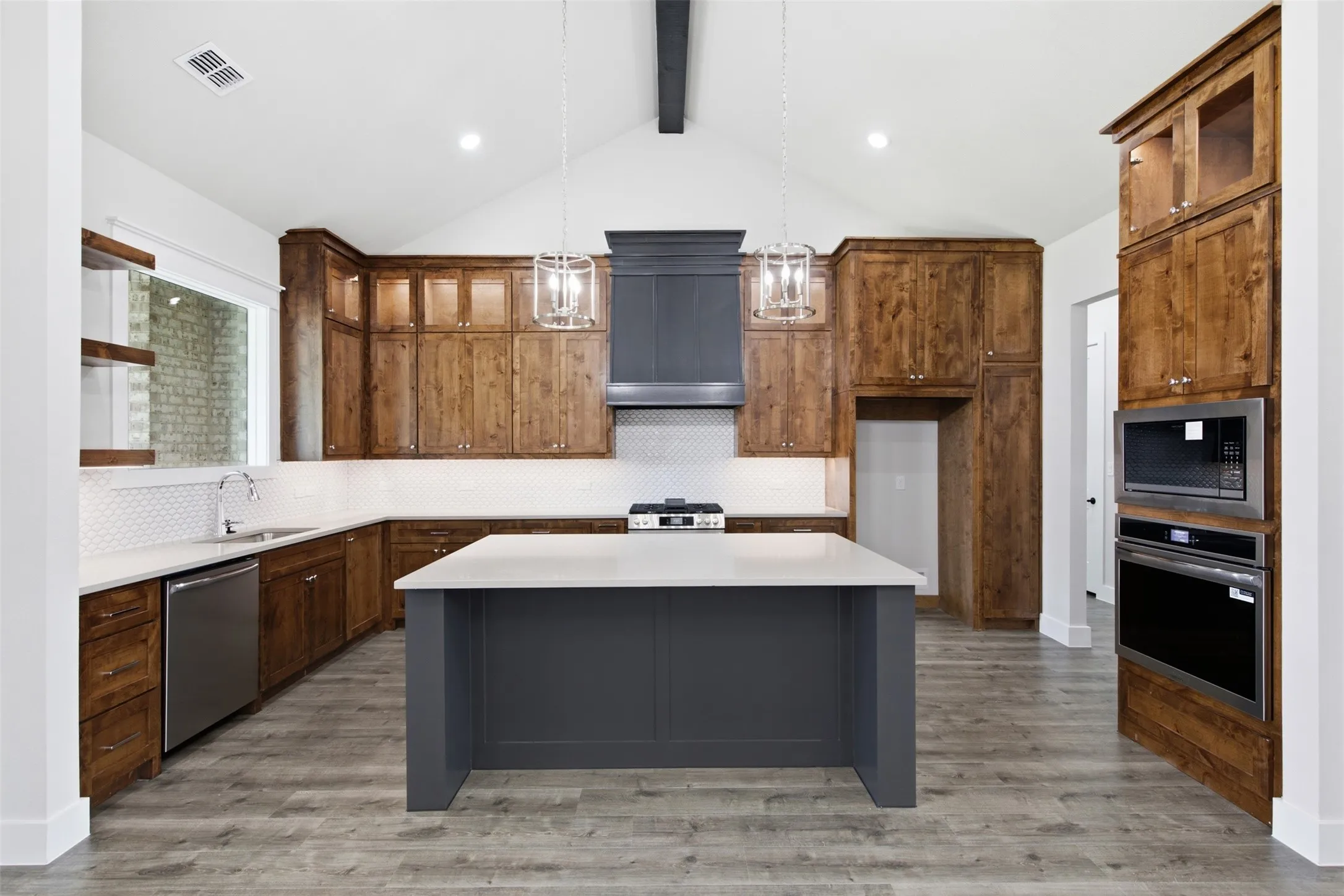 Spacious kitchen featuring a central island, wood-finish flooring, custom wood cabinetry, stainless steel appliances, and a vaulted ceiling with exposed beam