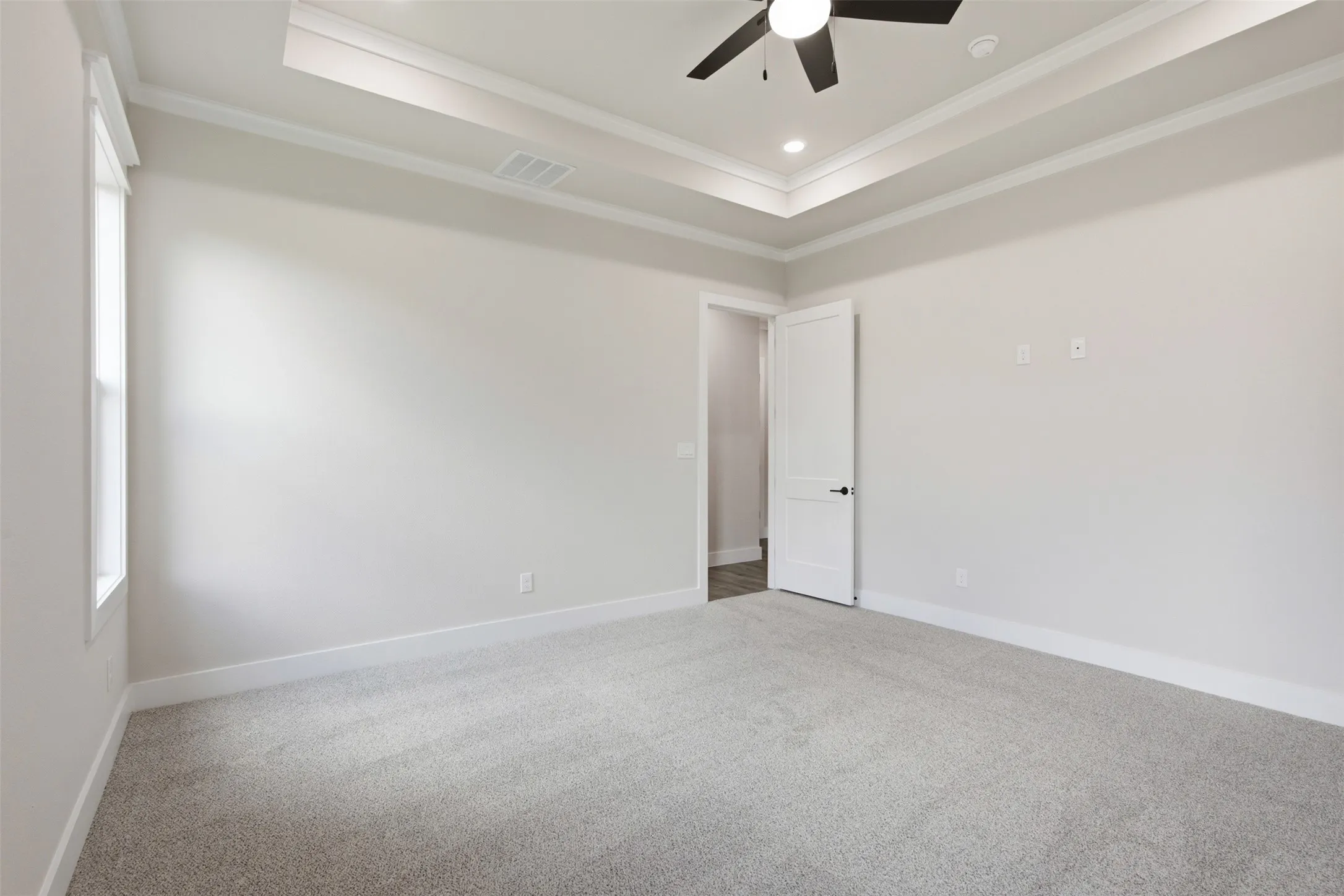 Spacious room featuring light gray carpeting, tray ceiling with recessed lighting, and a ceiling fan