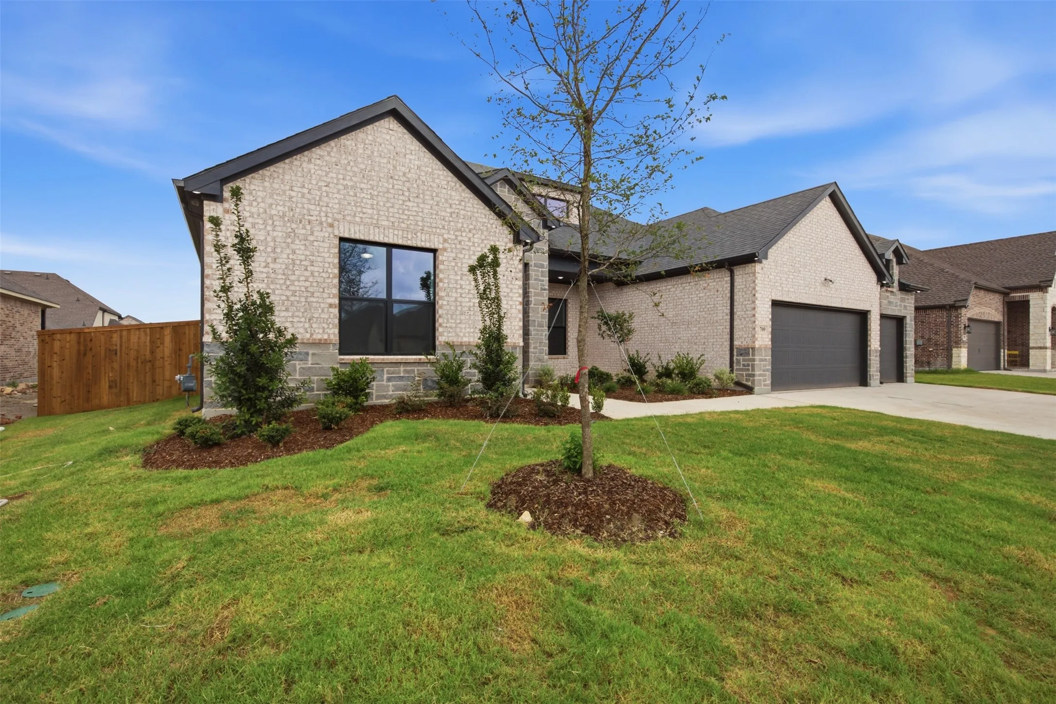 Contemporary brick exterior with stone accents, dark framed windows, a two-car garage, and a manicured lawn