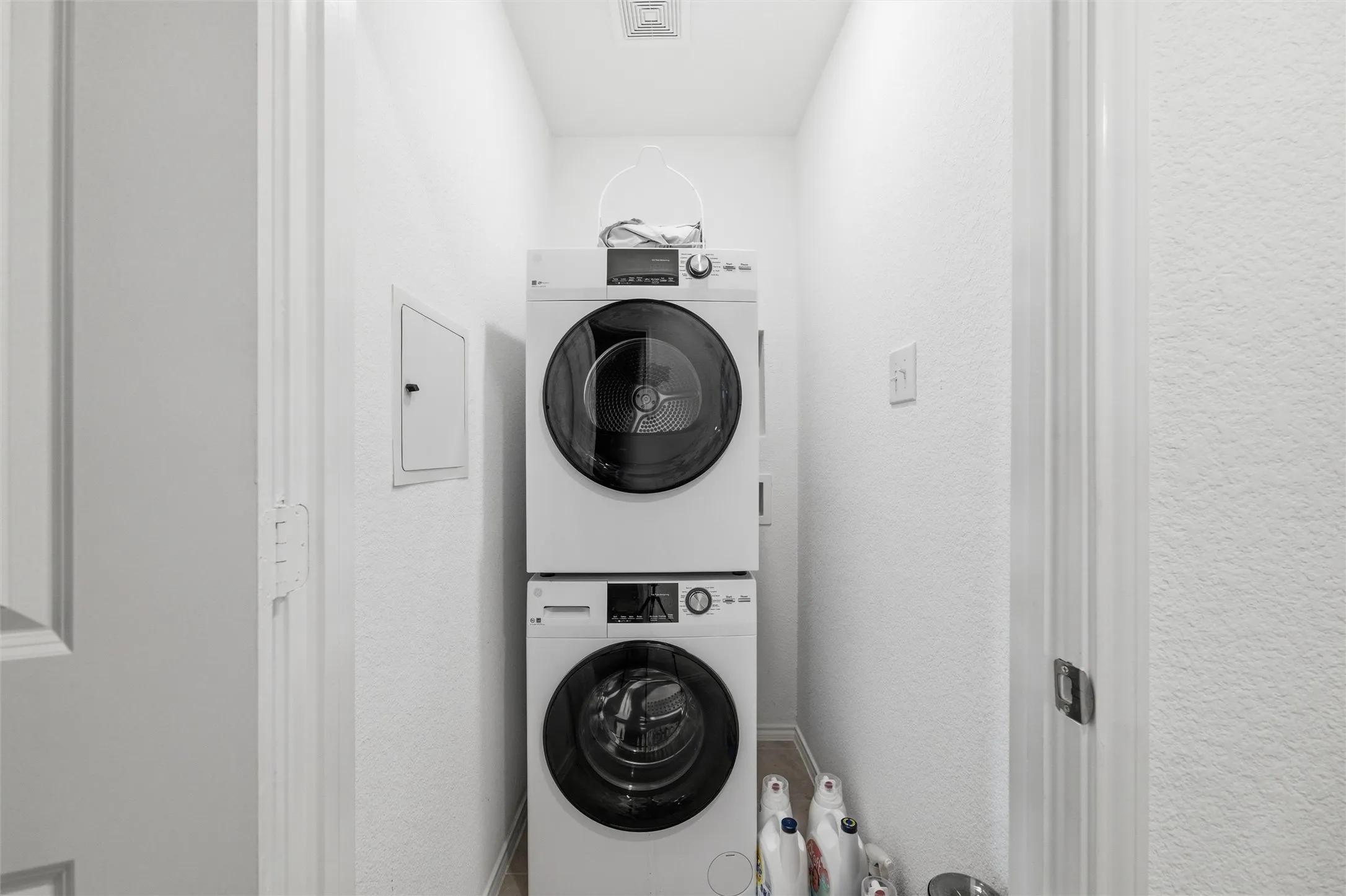 Laundry area with stacked washer and clothes dryer, a textured wall, and electric panel