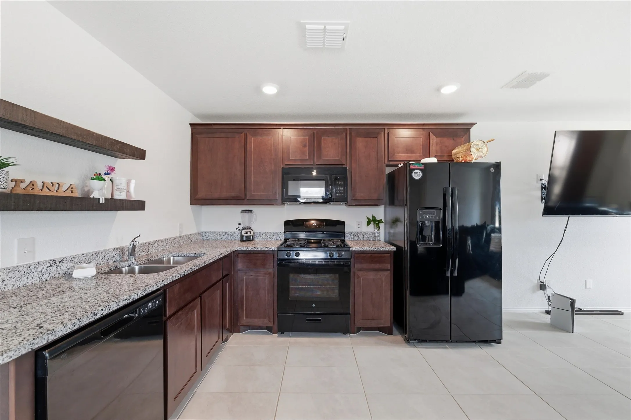 Kitchen with black appliances, open shelves, light stone countertops, dark wood finish cabinets, and light tile patterned flooring