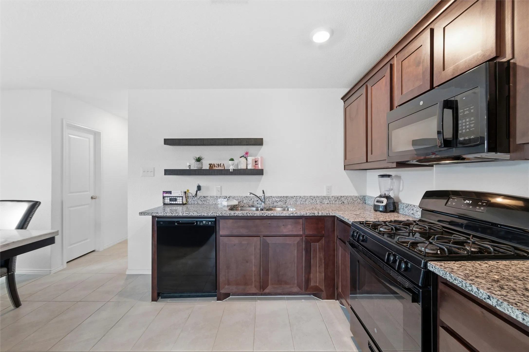 Kitchen with black appliances, light stone countertops, dark wood finish cabinetry, and open shelves