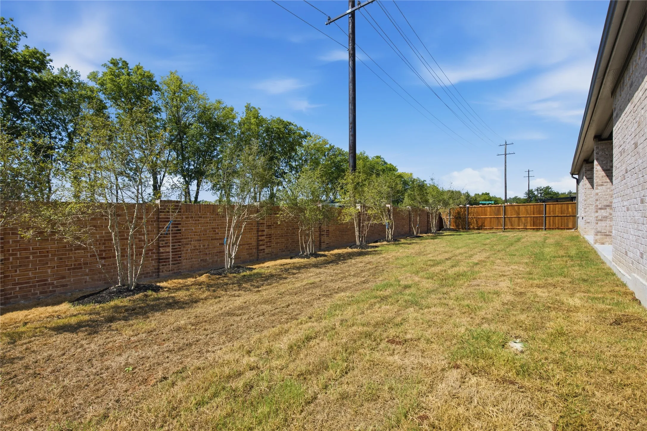 Expansive grassy yard with mature privacy trees, a brick perimeter wall, and a wood fence