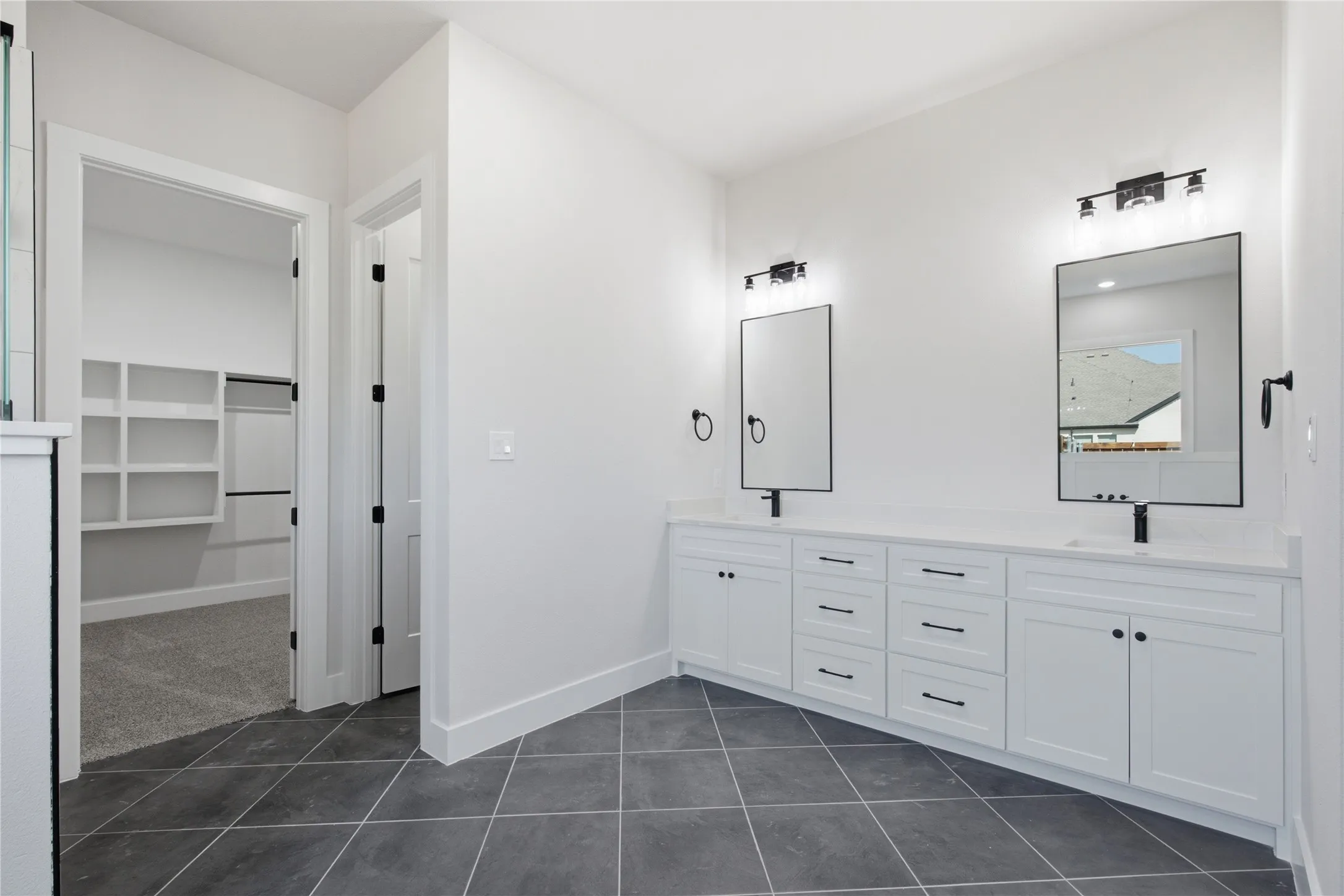 Spacious bath featuring dual vanities with white cabinetry, matte black hardware, and an expansive walk-in closet with built-in shelving