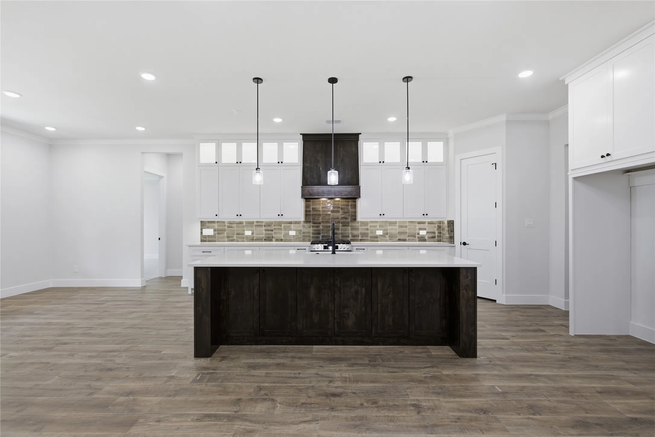 Kitchen featuring a dark wood-finish island with a white countertop, white upper and lower cabinetry, a mosaic tile backsplash, and three pendant lights