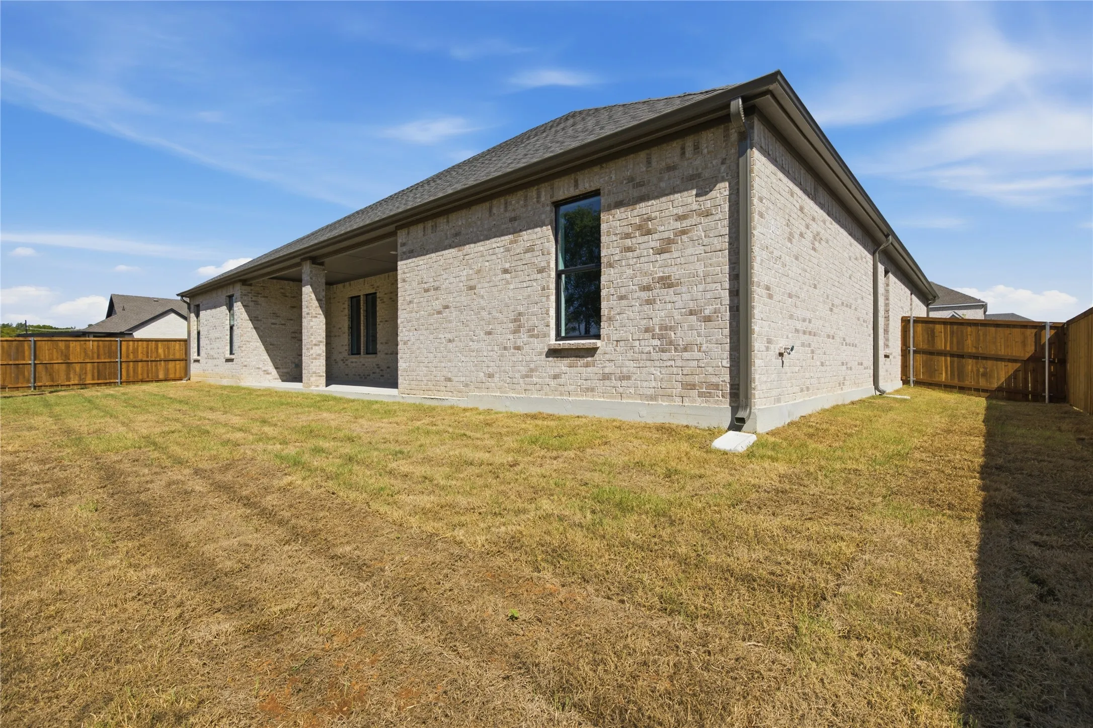 Brick exterior with a covered patio, dark shingle roof, and a wood fence enclosing the yard