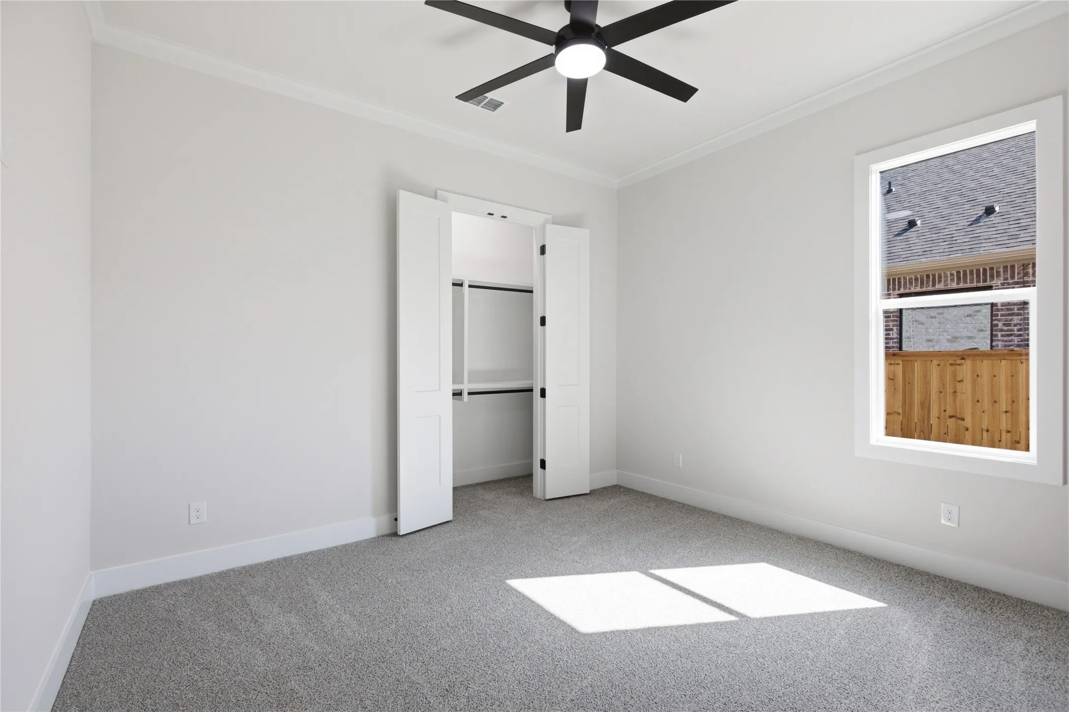 Recessed closet with bi-fold doors, grey carpeting, ceiling fan with integrated lighting, and a white-framed window