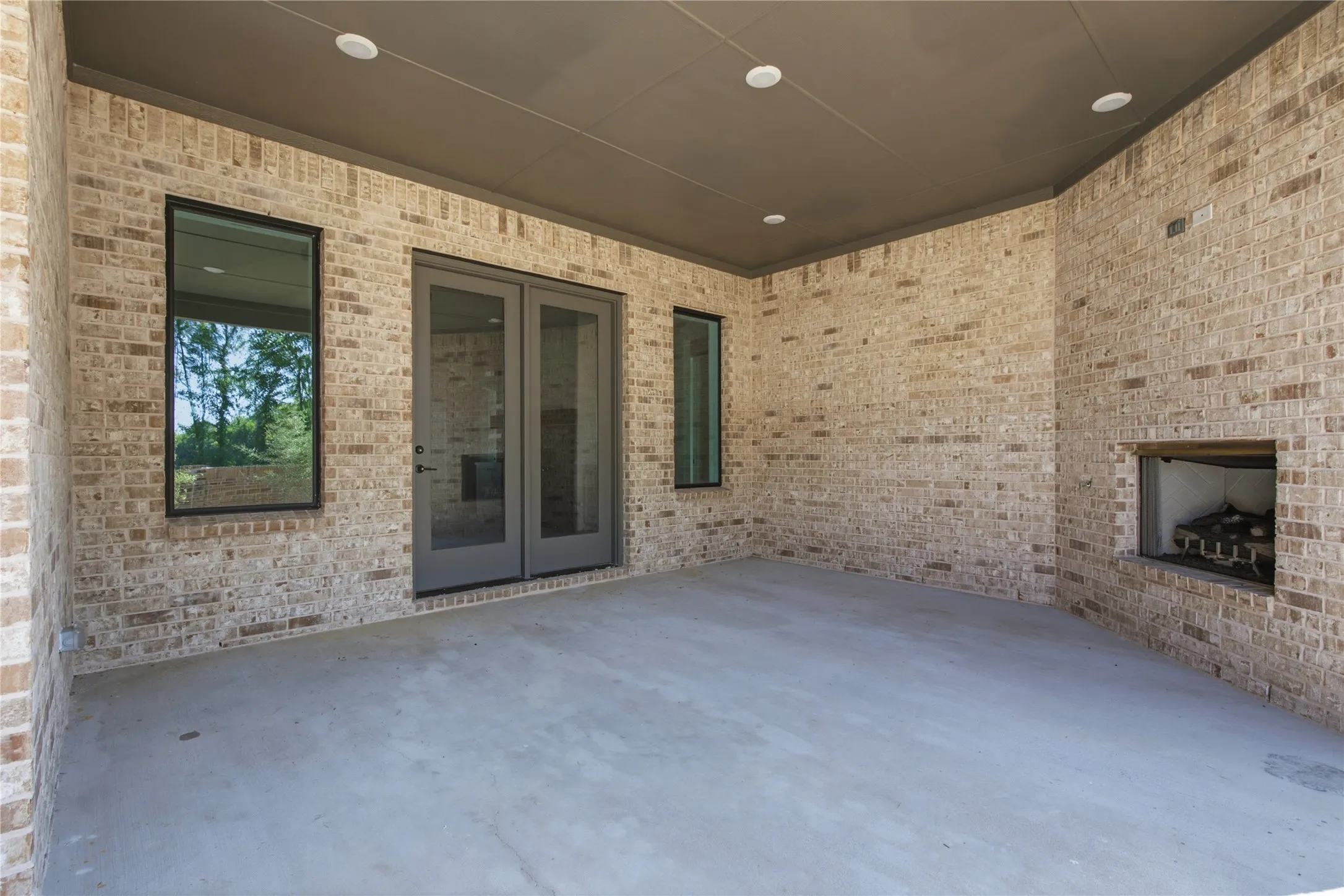 Covered outdoor patio featuring a brick exterior and a built-in outdoor fireplace