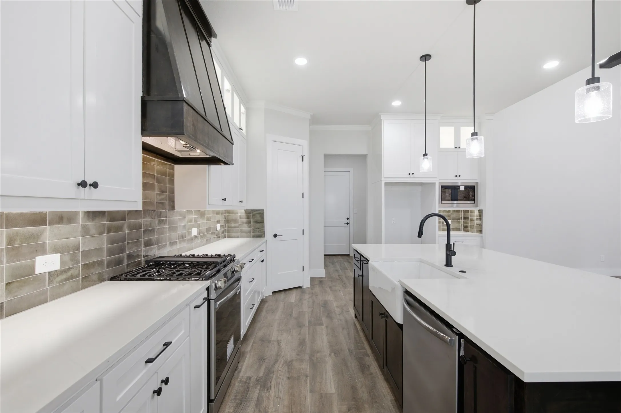 Spacious kitchen featuring white cabinetry, a large center island with a farmhouse sink, stainless steel appliances, and wood-finish flooring