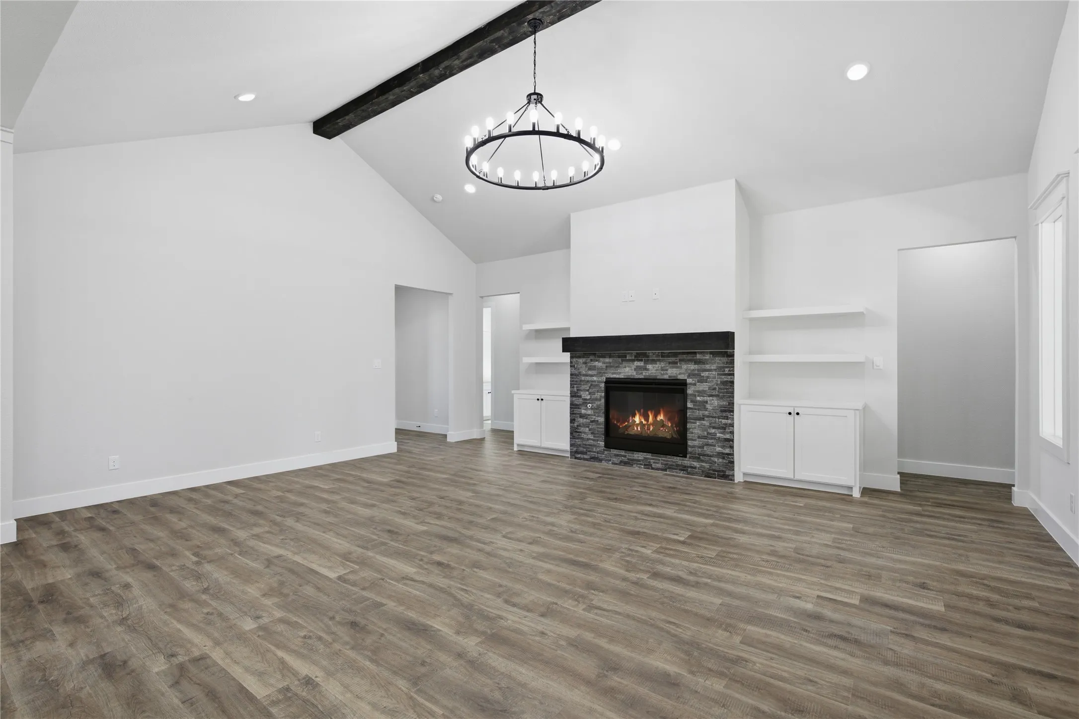 Vaulted ceiling with an exposed beam, wood-finish flooring, stone-clad fireplace with mantel, recessed lighting, and a circular chandelier