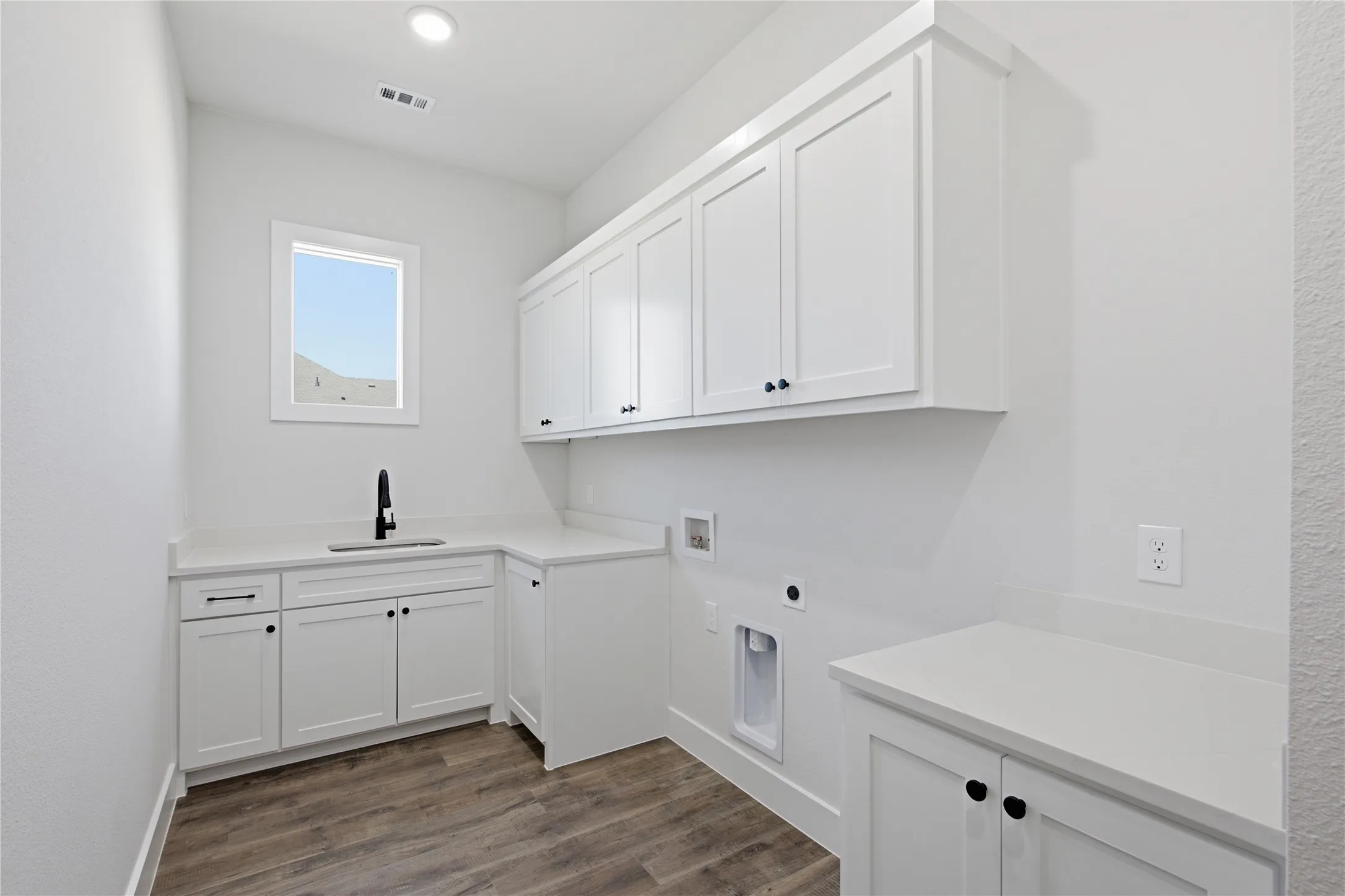 White cabinetry with black hardware, wood-finish flooring, undermount sink with a black pull-down faucet, and light-toned countertops