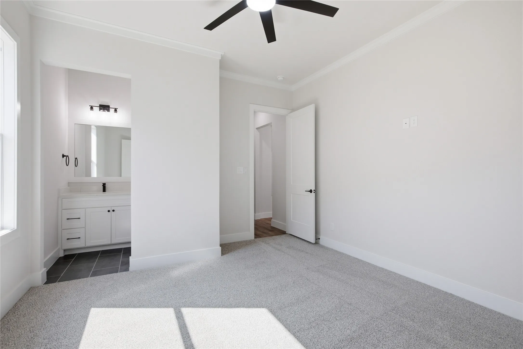 Plush carpet flooring, crown molding, ceiling fan, white paneled door, and a vanity with a white cabinet and dark tile flooring