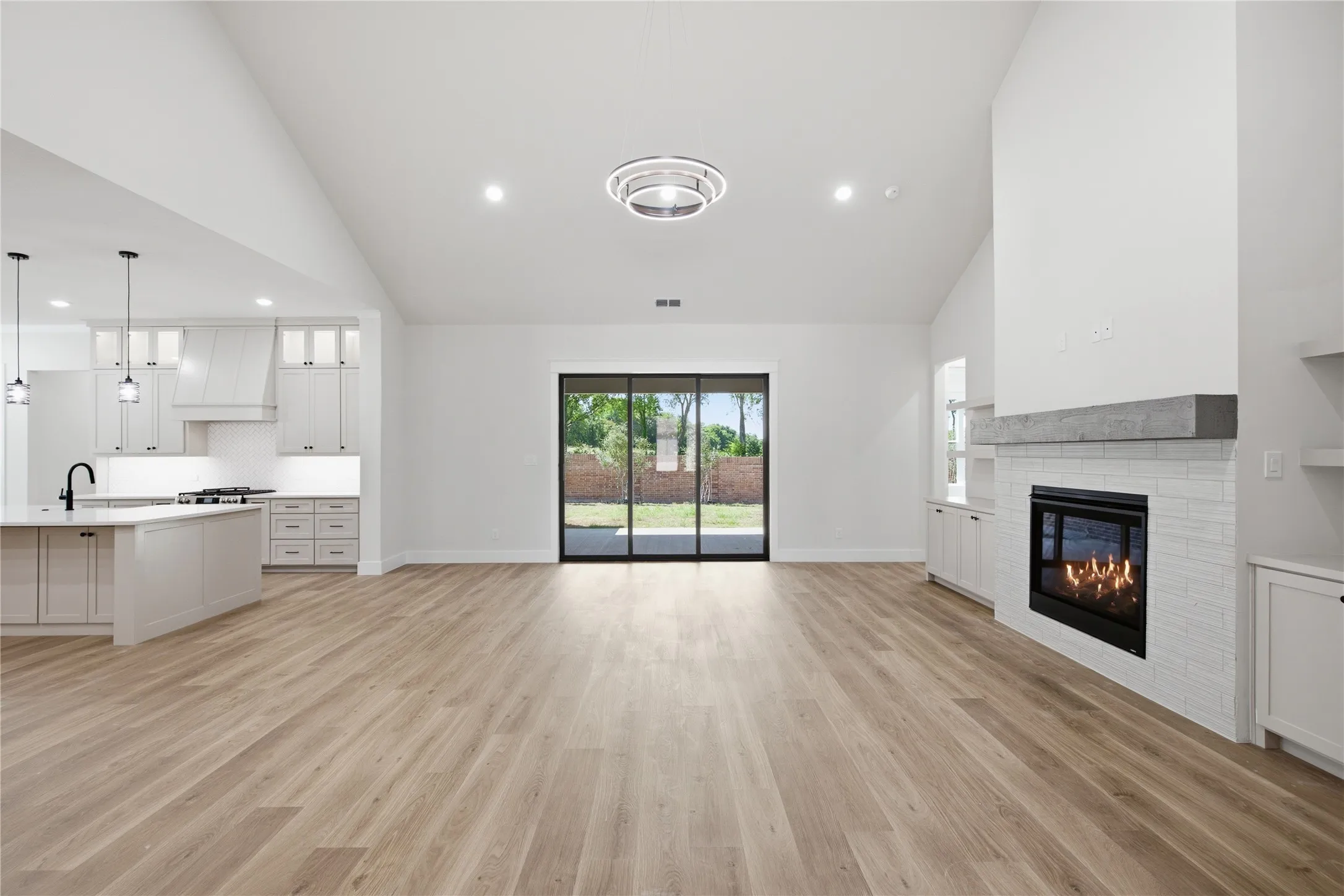 Vaulted ceilings, wood-finish flooring, white cabinetry, built-in fireplace with a tile surround, and sliding glass doors to the exterior