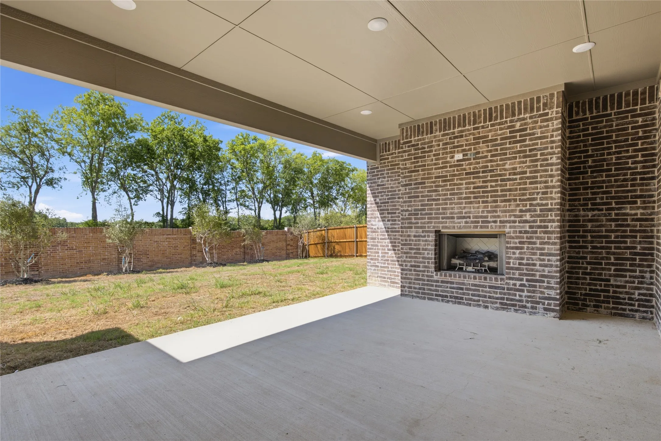 Covered patio with a brick fireplace and recessed lighting
