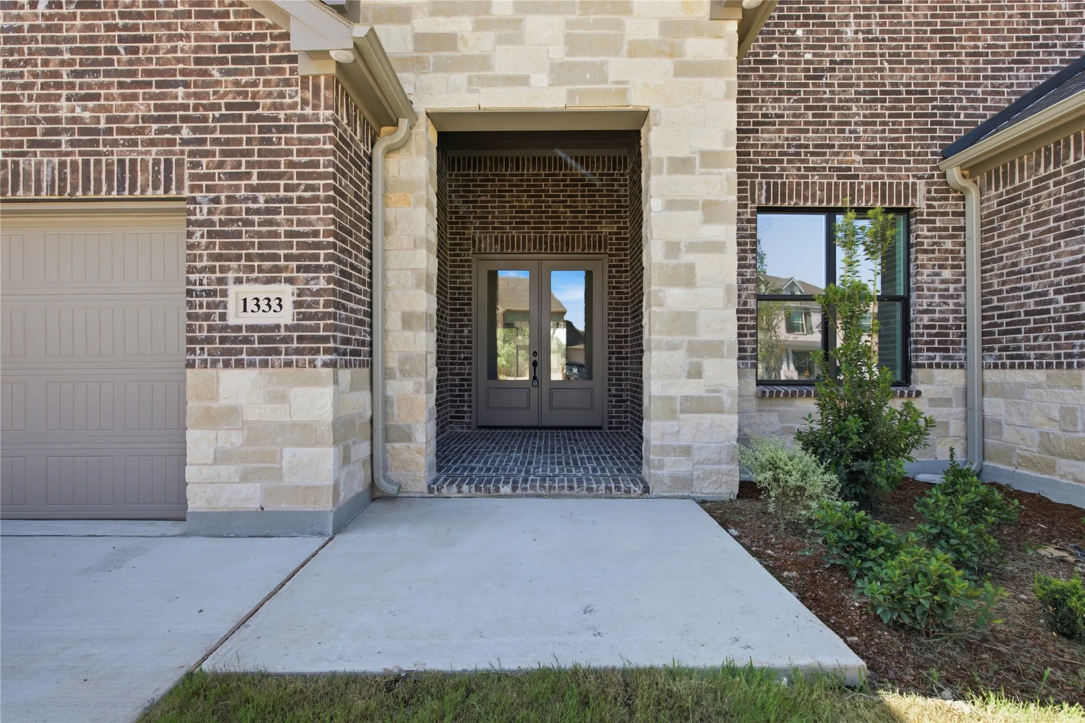 Brick and stone facade, double entry doors, paved entryway, and a concrete driveway
