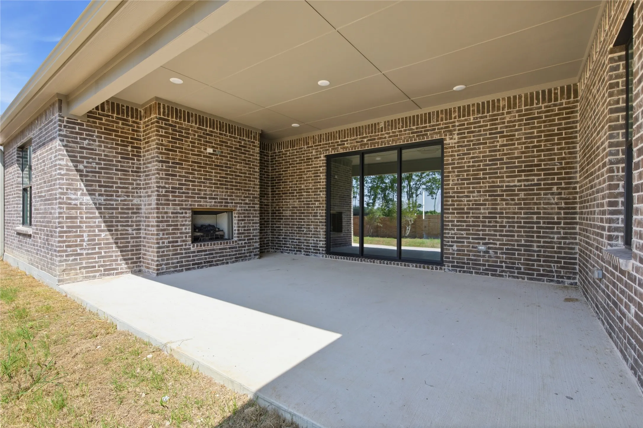 Covered patio featuring brick construction, recessed lighting, an outdoor fireplace, and sliding glass doors