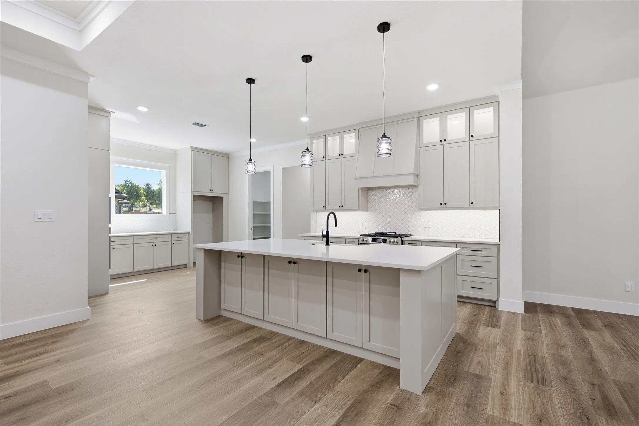 Wood-finish flooring throughout, white shaker cabinetry, white countertops, built-in range, and contemporary pendant lighting