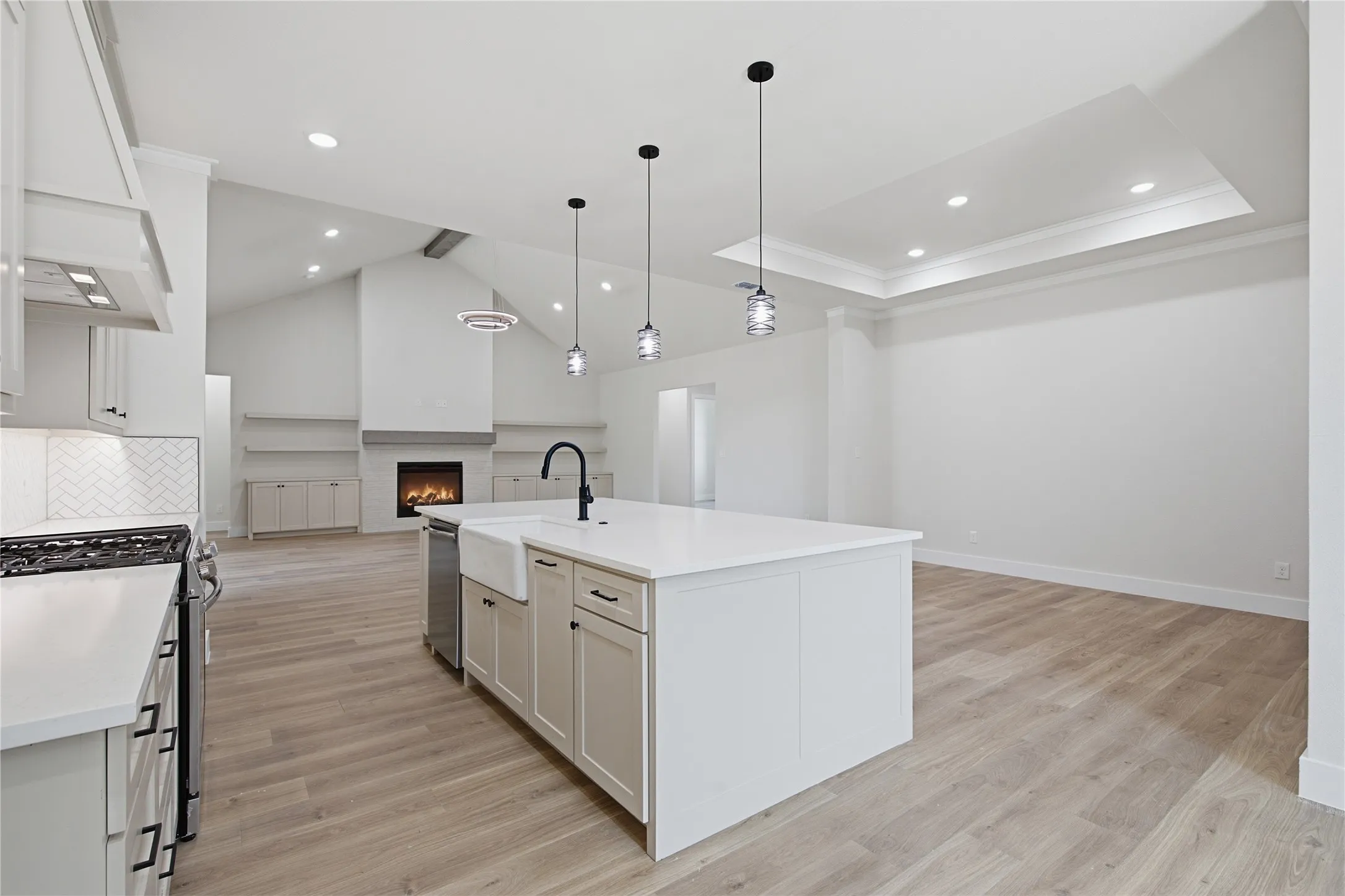 Spacious kitchen island with an integrated farmhouse sink and matte black faucet, complemented by light wood-finish flooring