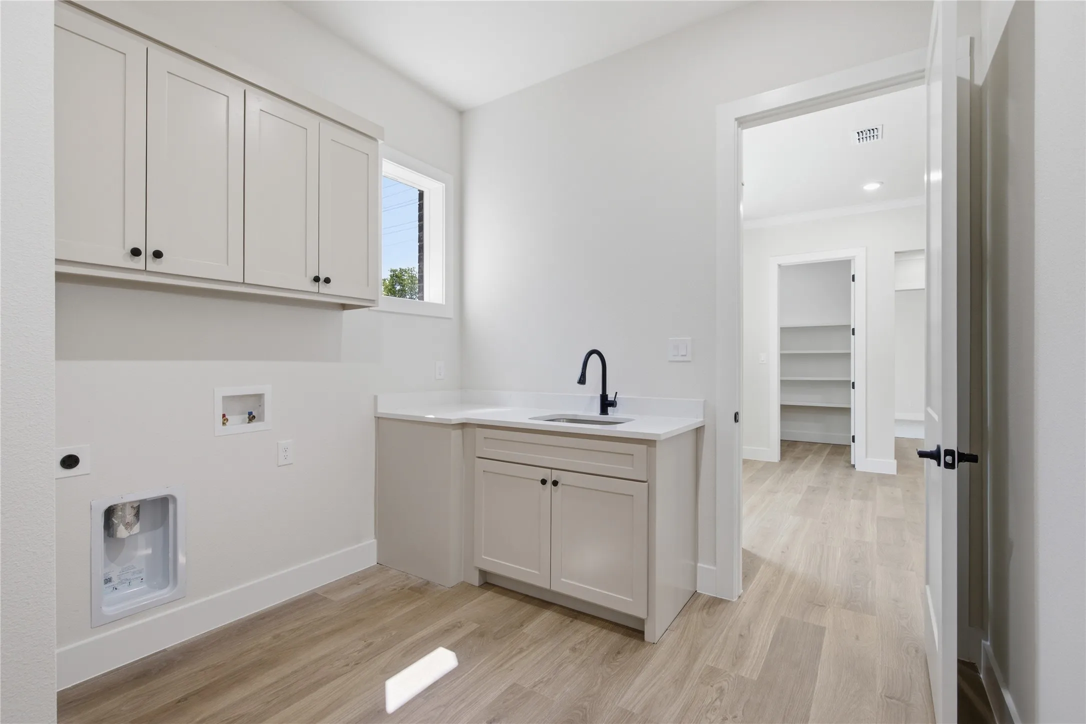 Light wood-finish flooring, white cabinetry with black hardware, white countertop, and a black gooseneck faucet