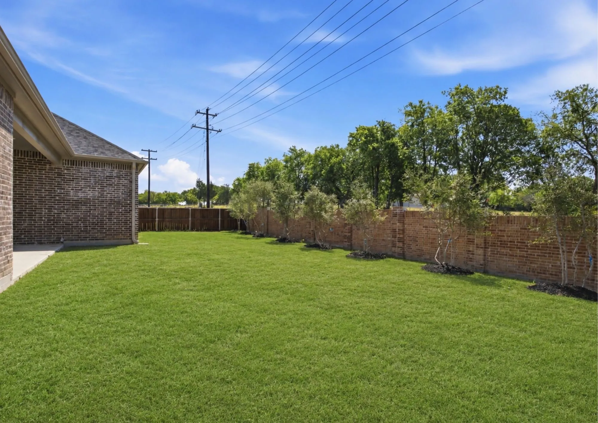 AI Enhanced. Expansive green lawn bordered by a brick privacy wall and mature trees