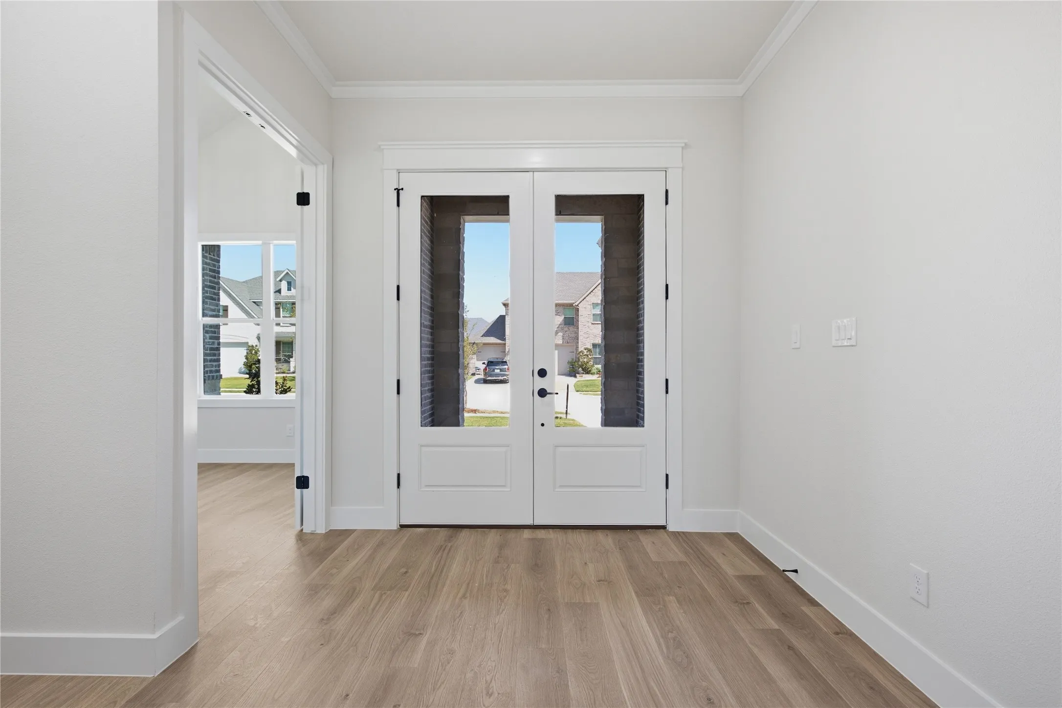 Double entry doors with integrated glass panels, wood-finish flooring, white trim, and crown molding