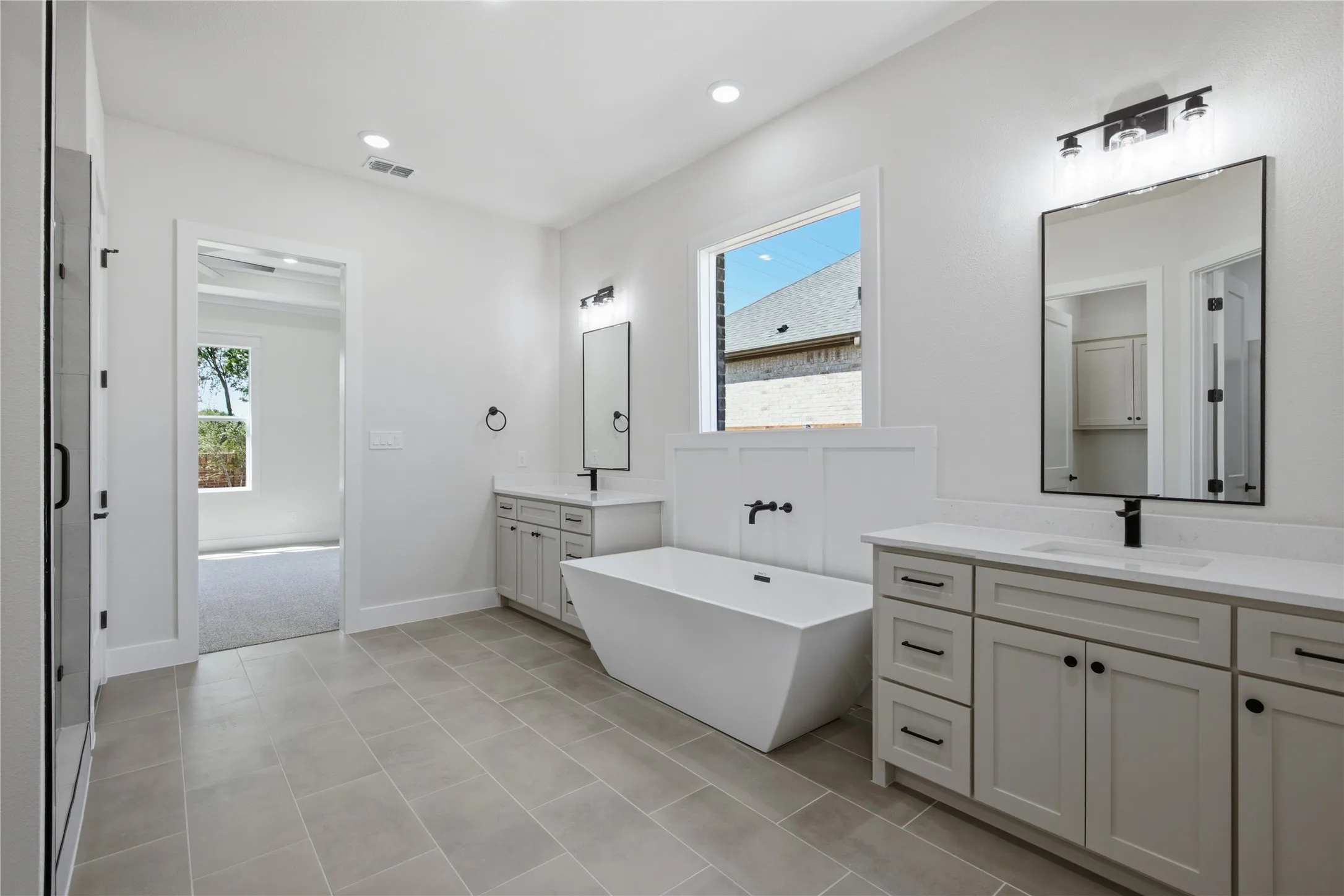 Spacious bathroom featuring a freestanding soaking tub with wall-mounted fixtures, dual vanities with undermount sinks and quartz countertops, and large format tile flooring