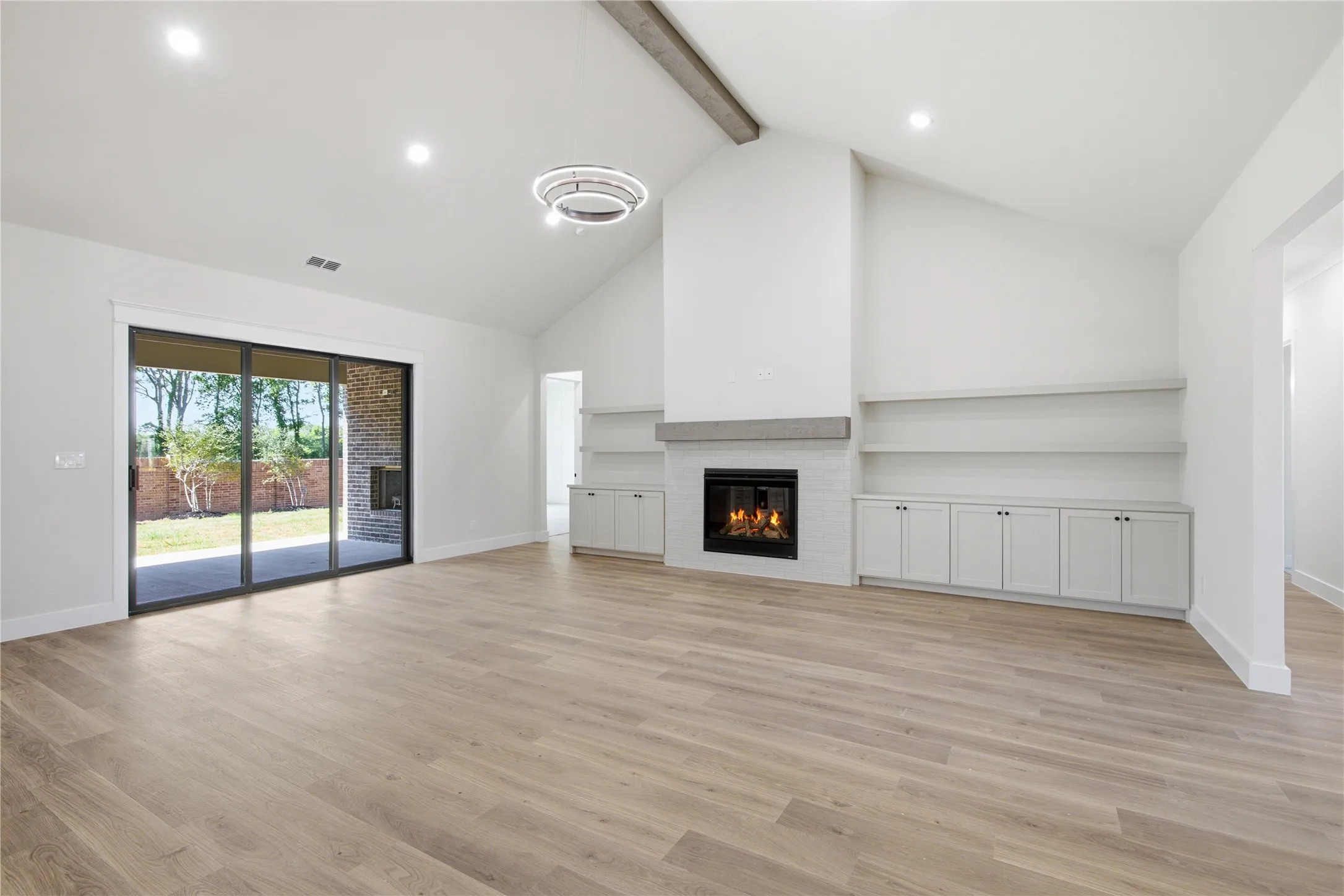 Vaulted ceiling with exposed beam, wood-finish flooring, built-in shelving and cabinetry, fireplace with hearth, and sliding glass doors