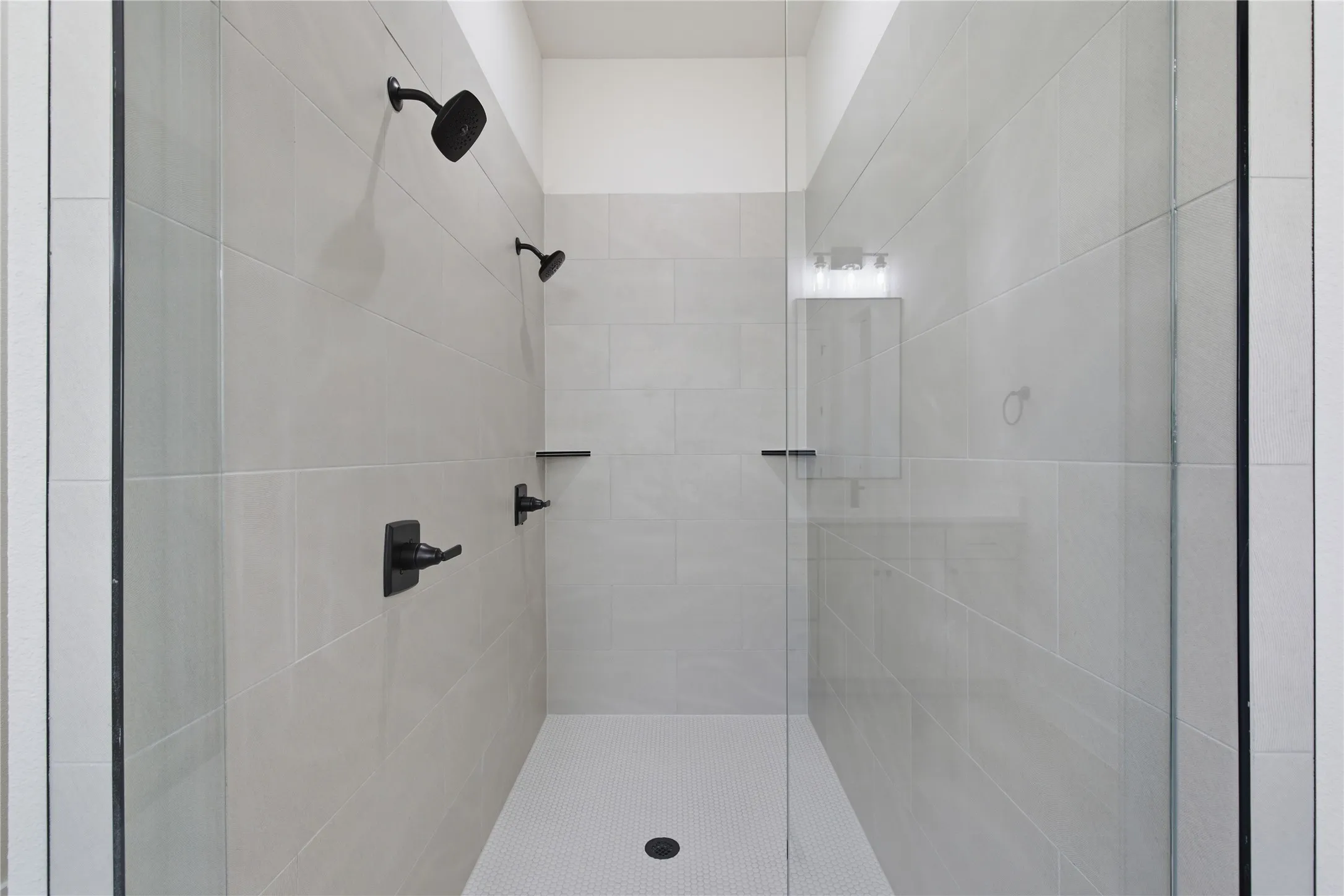 Walk-in shower featuring light-toned tile walls and a white hexagonal tile floor