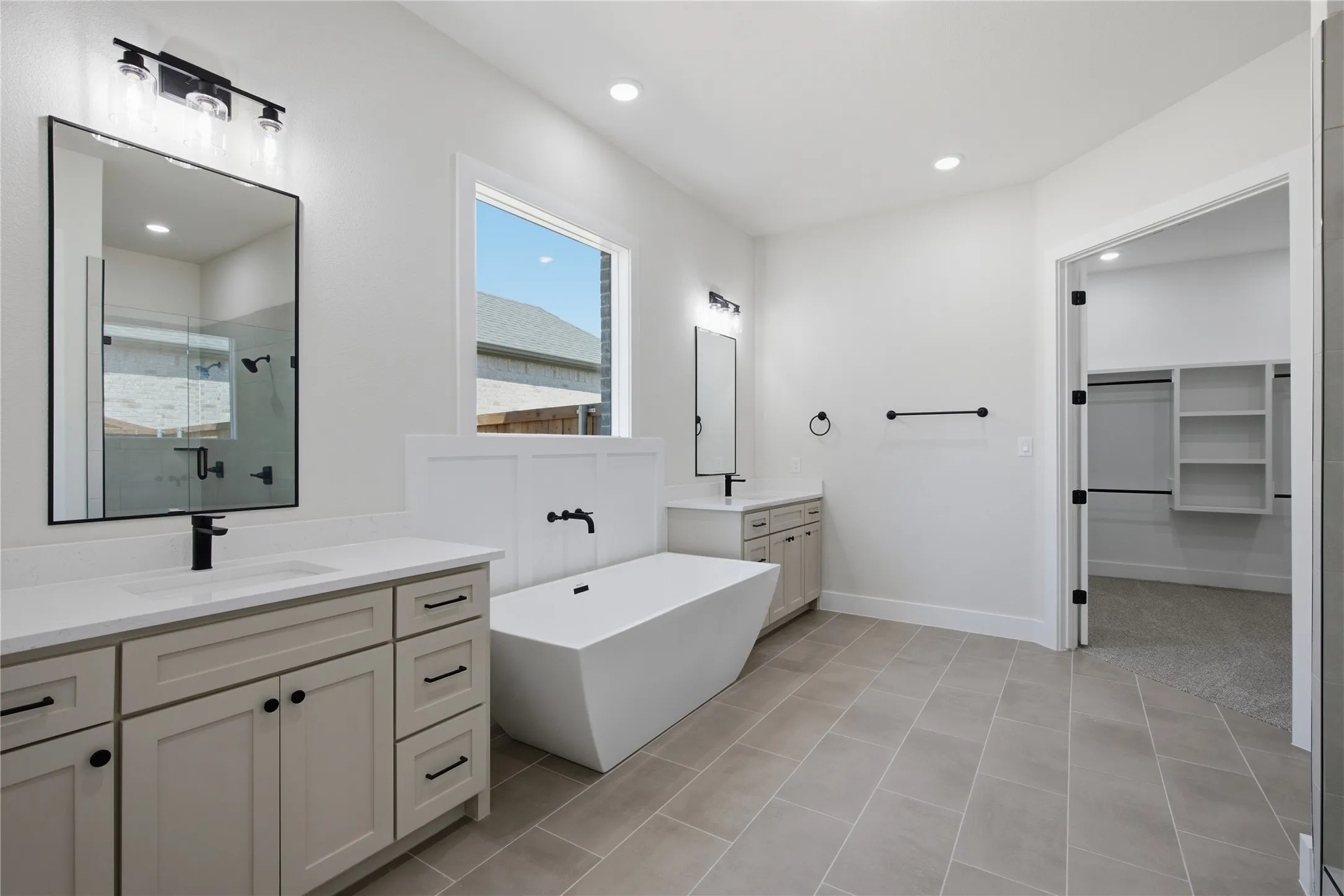 Dual vanity with quartz countertops, a freestanding soaking tub, a walk-in shower with glass enclosure, and large-format tile flooring