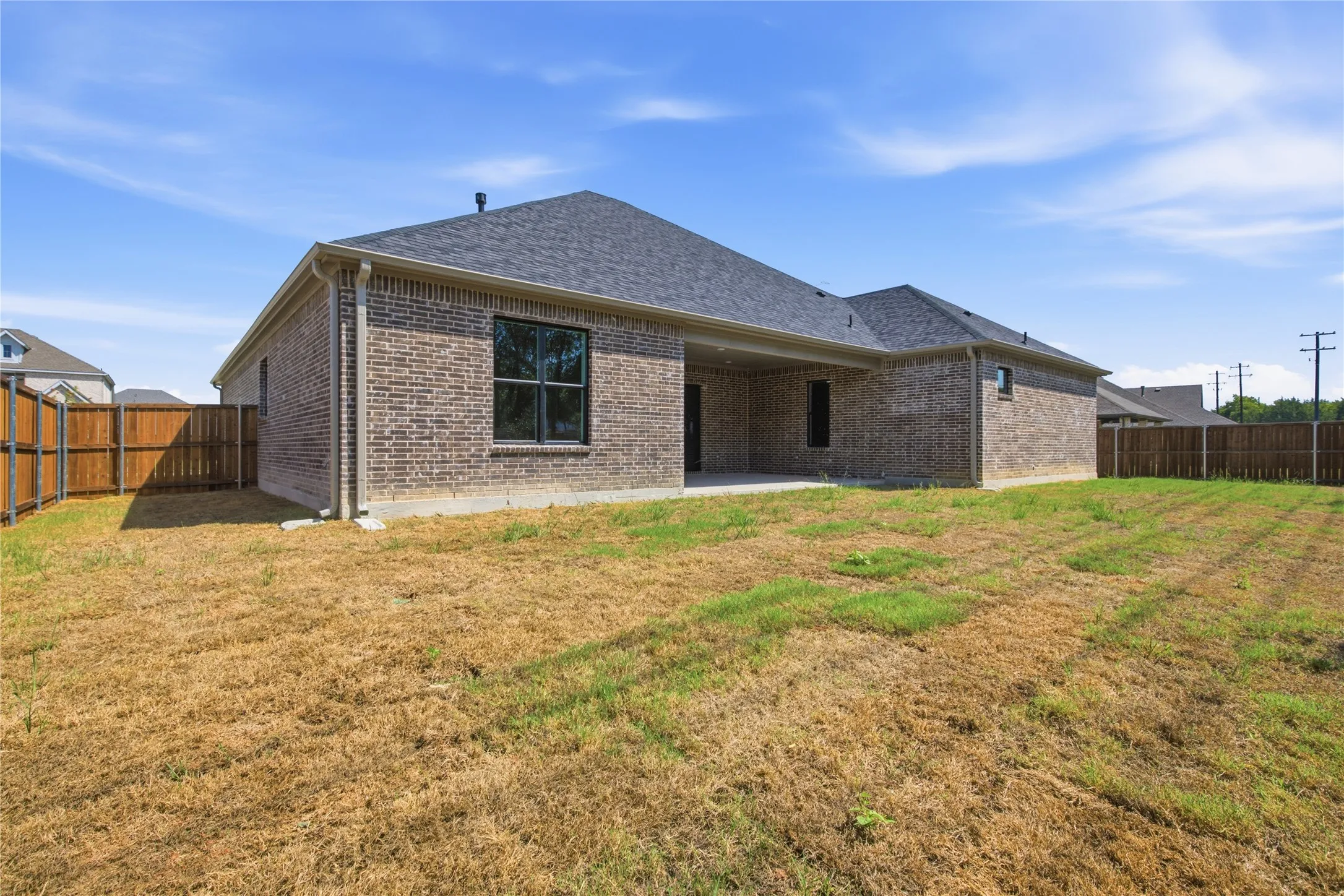 Brick exterior with black-framed windows, an attached covered patio, and a privacy fence