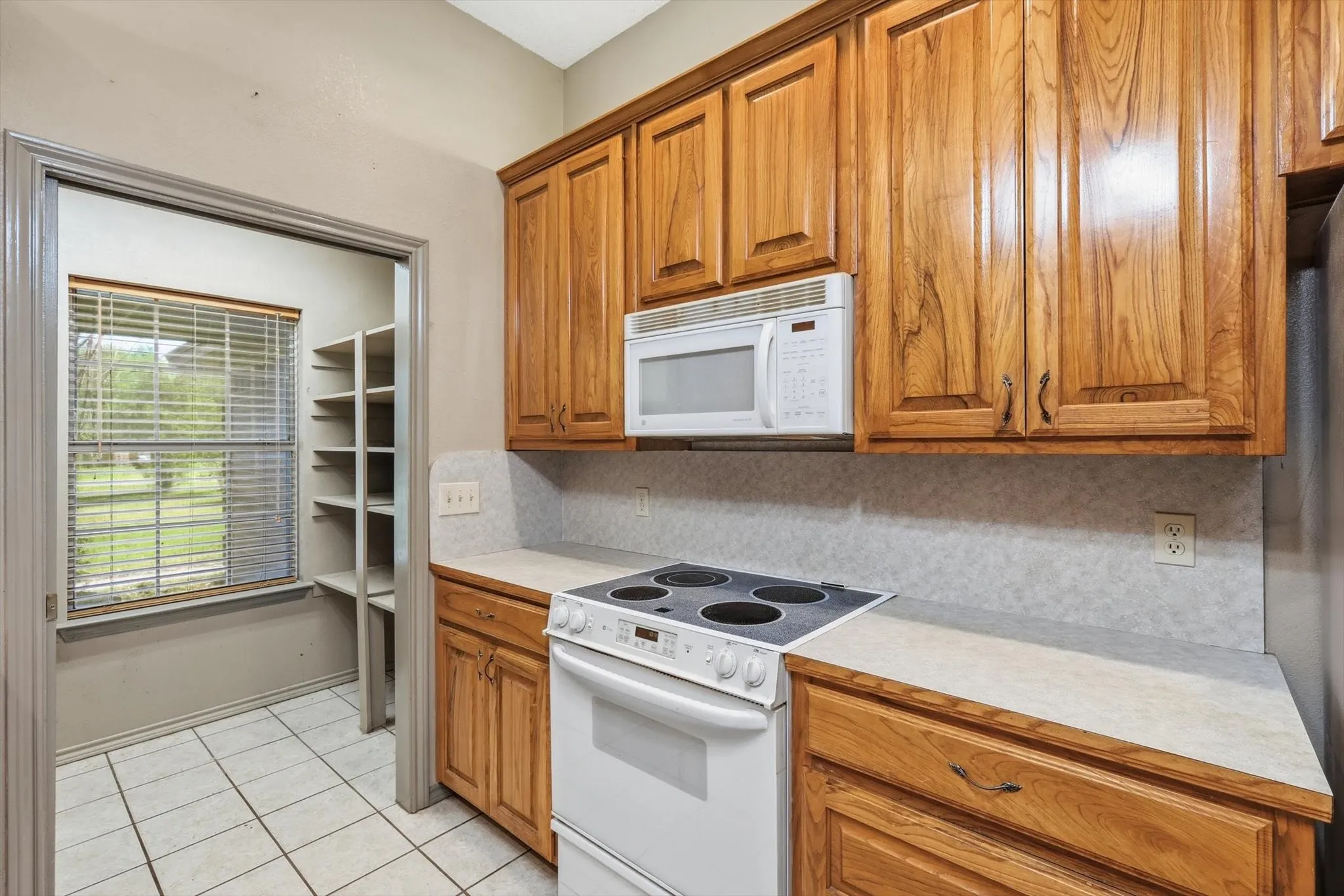 Kitchen featuring light countertops, white appliances, light tile patterned floors, wood finish cabinets, and decorative backsplash