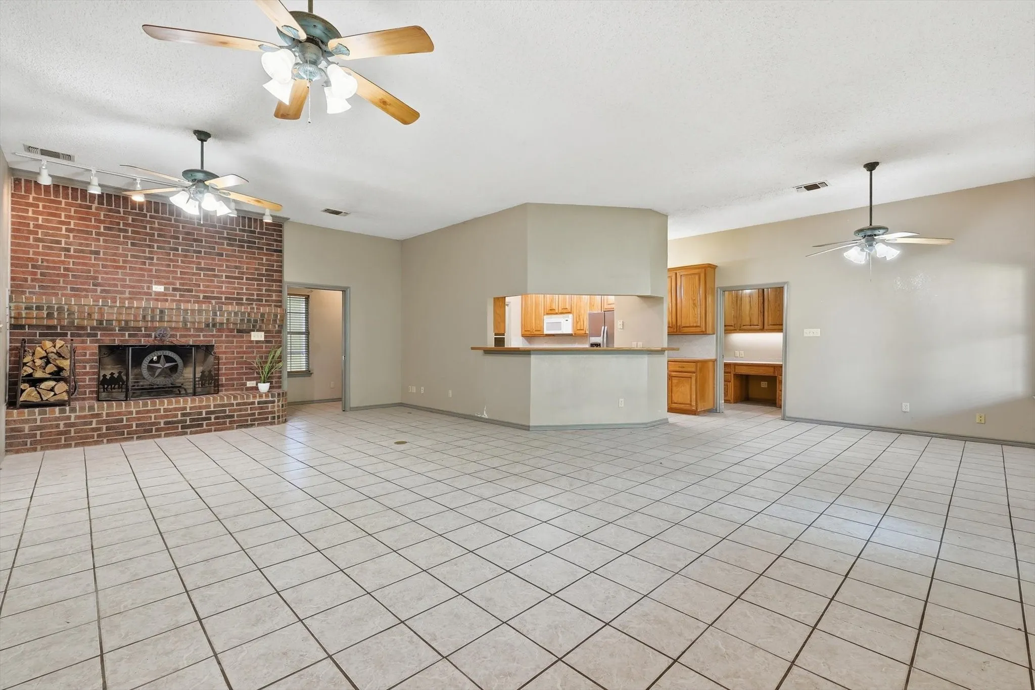 Unfurnished living room with a ceiling fan, light tile patterned flooring, a brick fireplace, rail lighting, and a textured ceiling