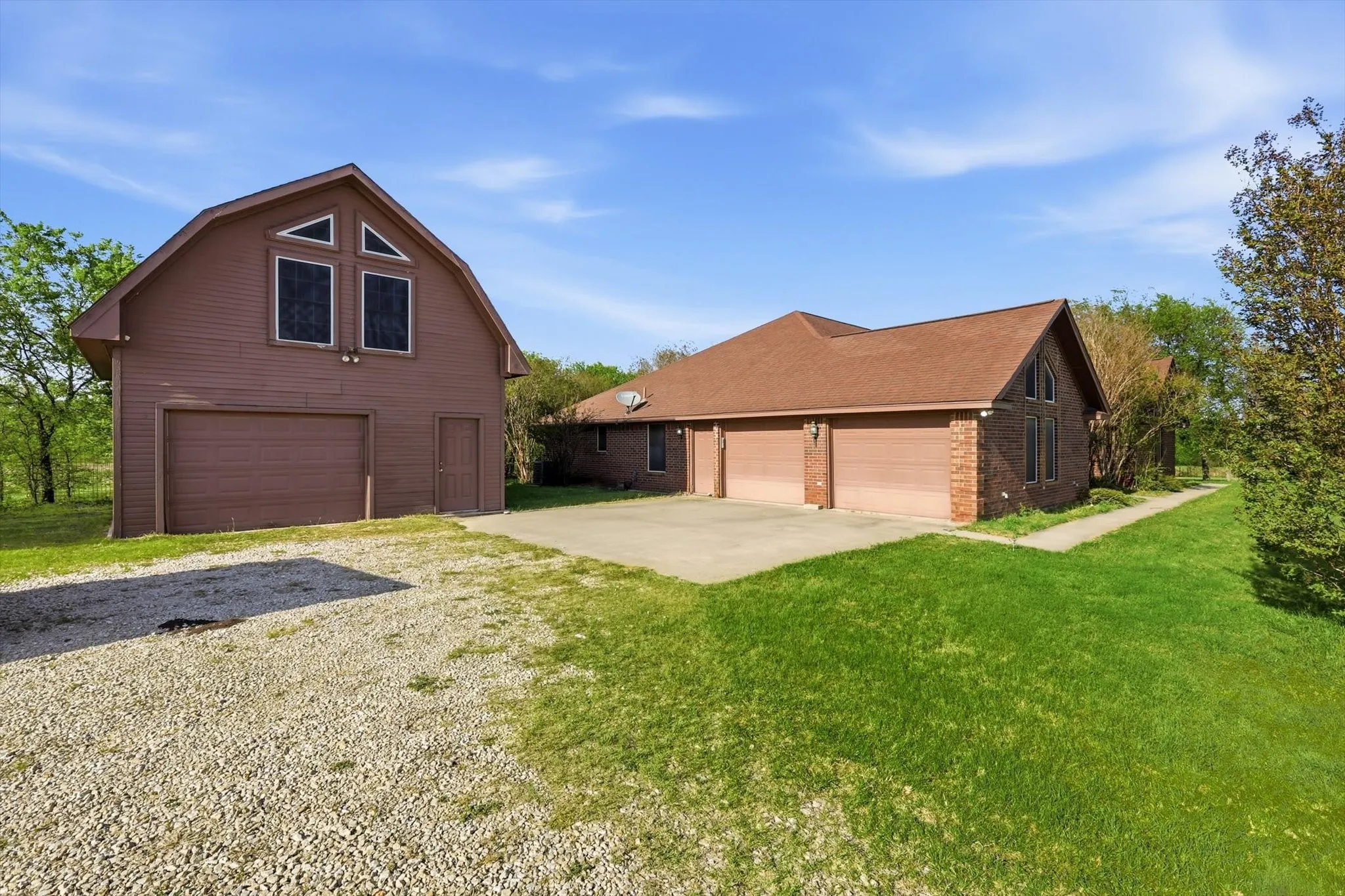 View of front of house with a detached garage, brick siding, driveway, a front lawn, and a gambrel roof