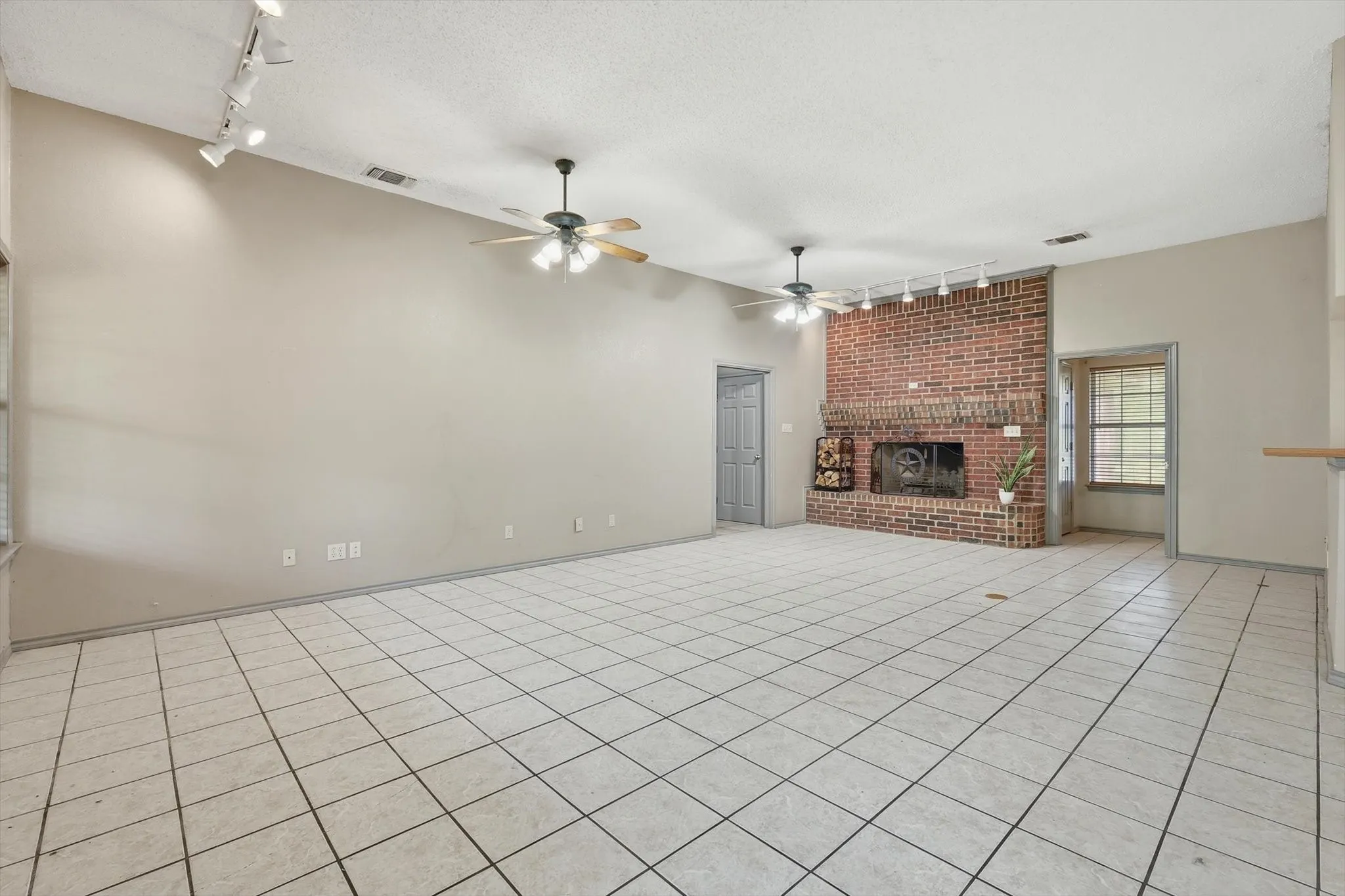 Unfurnished living room featuring track lighting, a textured ceiling, a fireplace, light tile patterned floors, and a ceiling fan