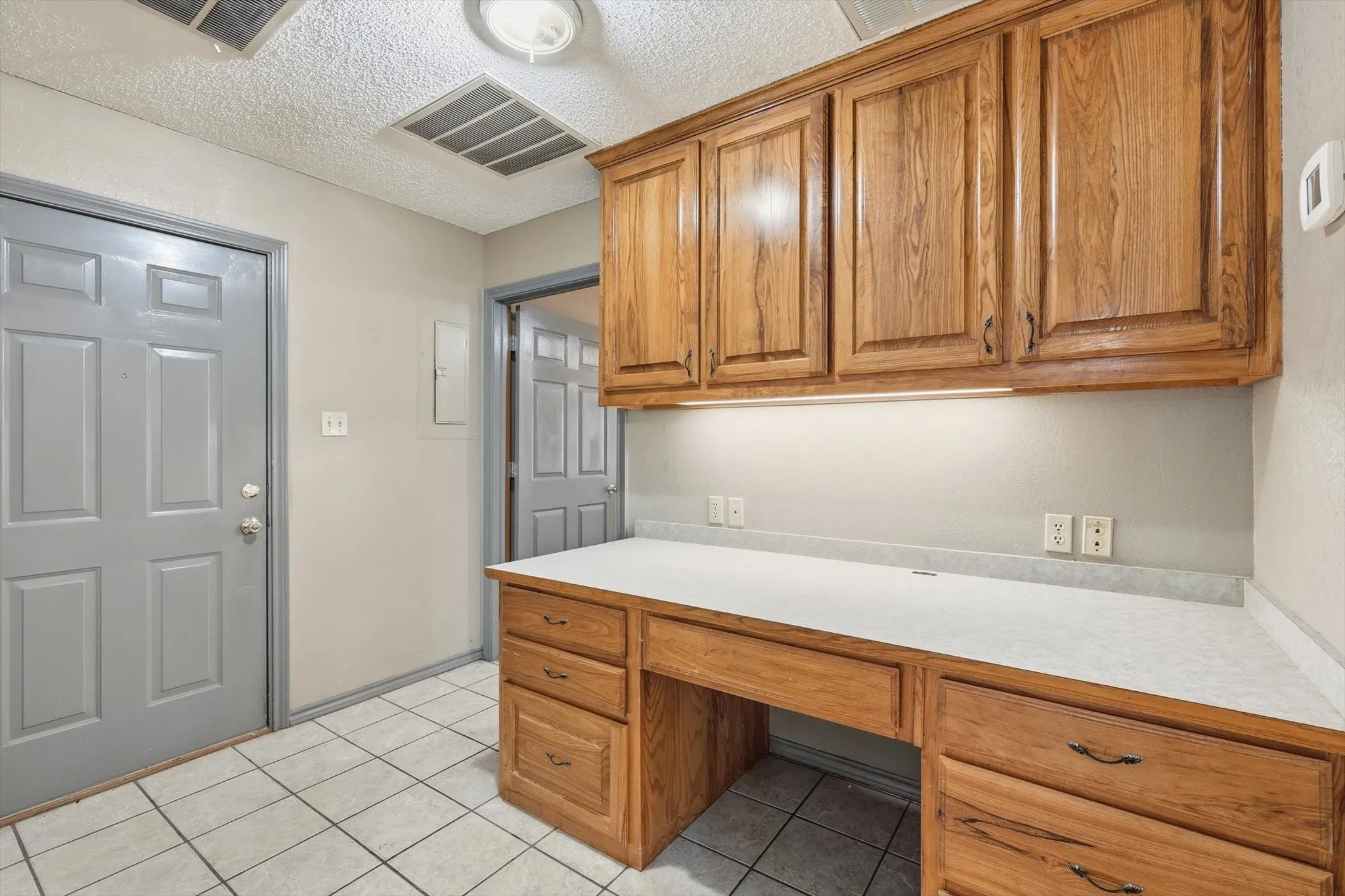 Unfurnished office featuring a textured ceiling, built in desk, and light tile patterned floors