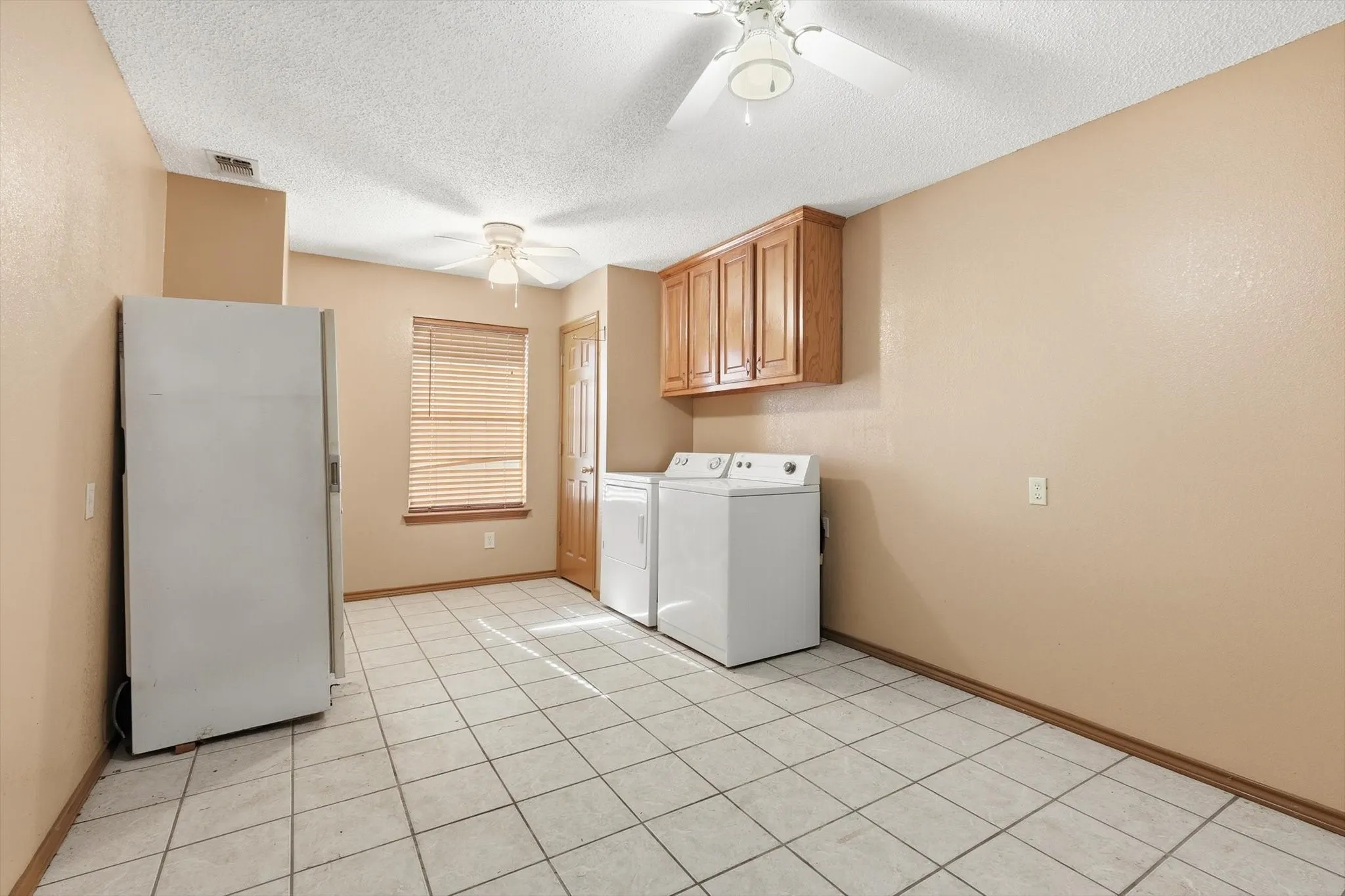 Laundry room featuring washing machine and dryer, a textured ceiling, ceiling fan, light tile patterned floors, and cabinet space