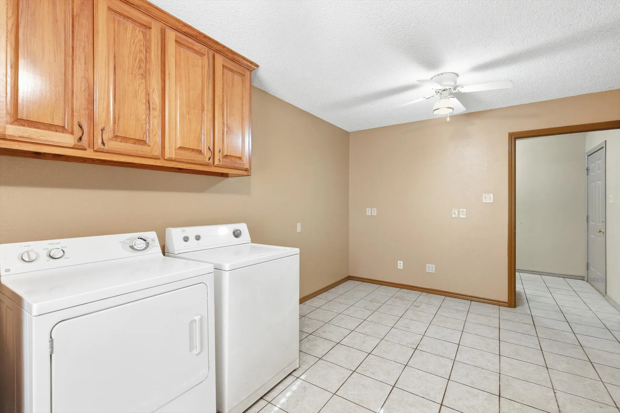 Laundry area with a ceiling fan, washing machine and clothes dryer, a textured ceiling, and light tile patterned floors