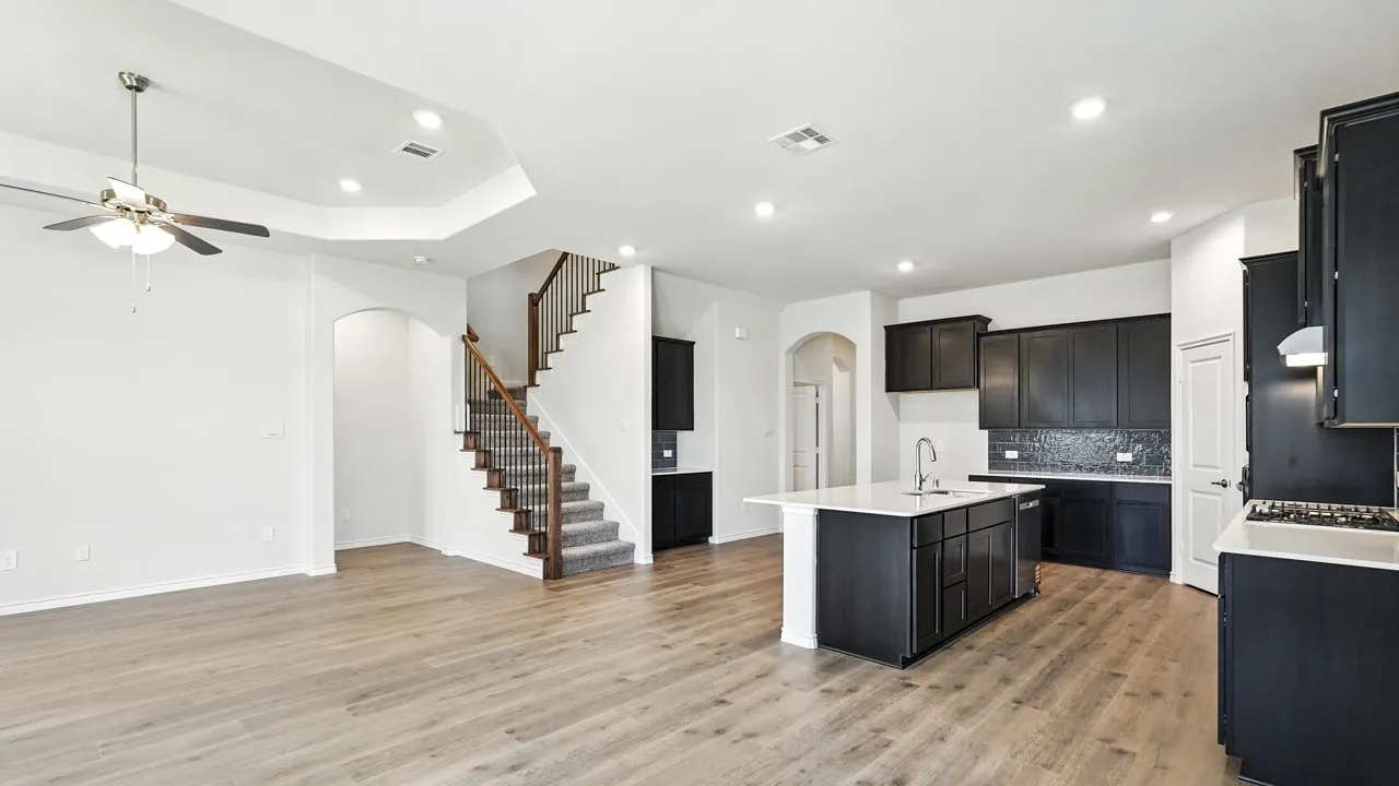 Kitchen with arched walkways, dark cabinetry, a center island with sink, open floor plan, and recessed lighting