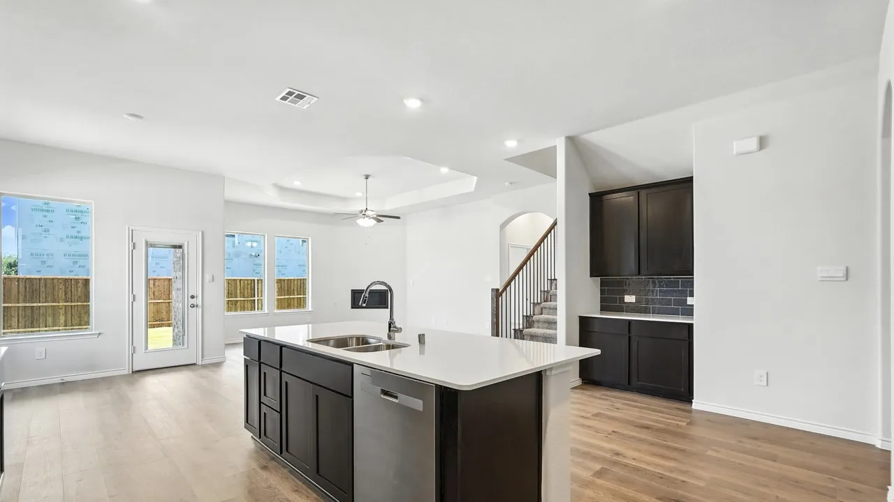 Kitchen with dishwasher, arched walkways, a center island with sink, light wood-style flooring, and light stone countertops