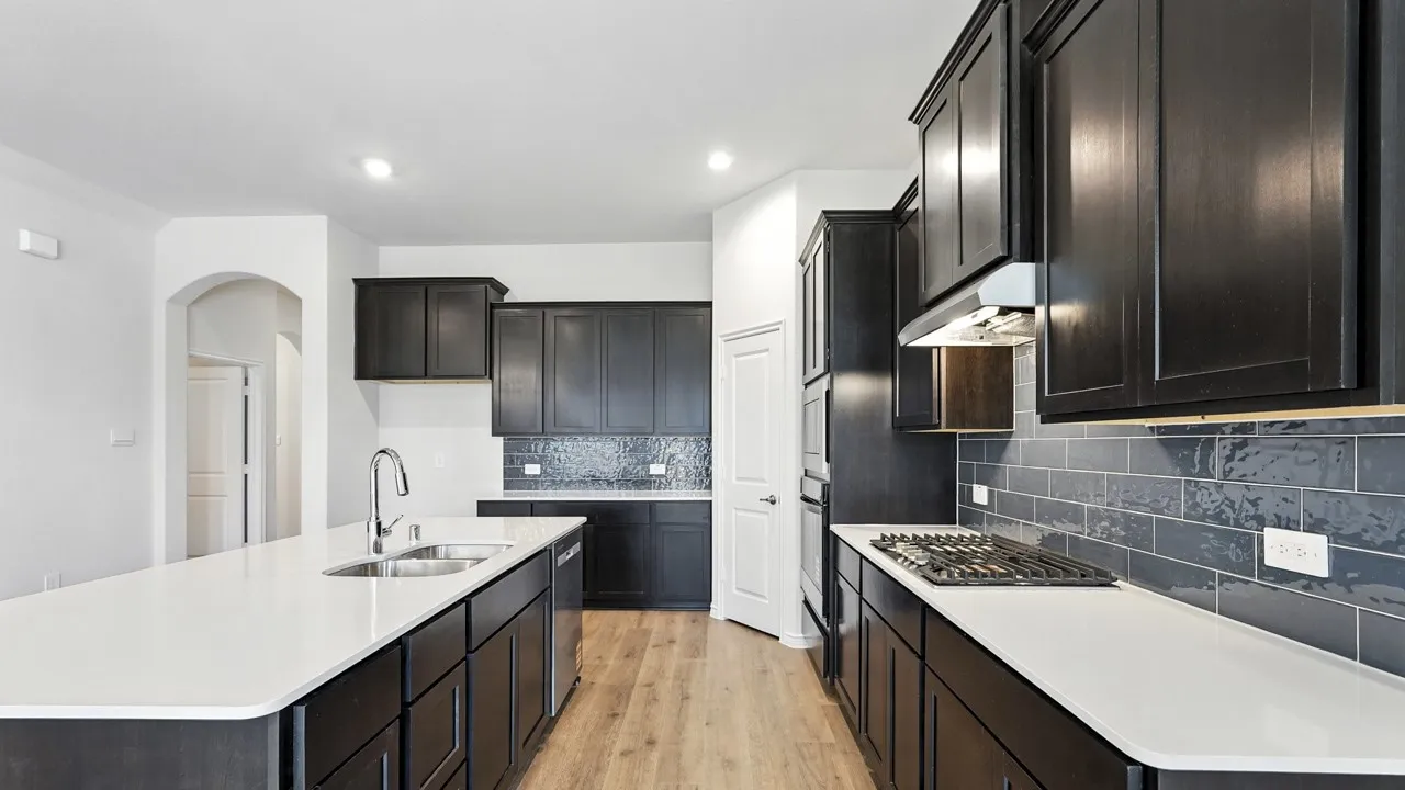 Kitchen featuring light wood-style flooring, a center island with sink, decorative backsplash, light stone counters, and stainless steel appliances