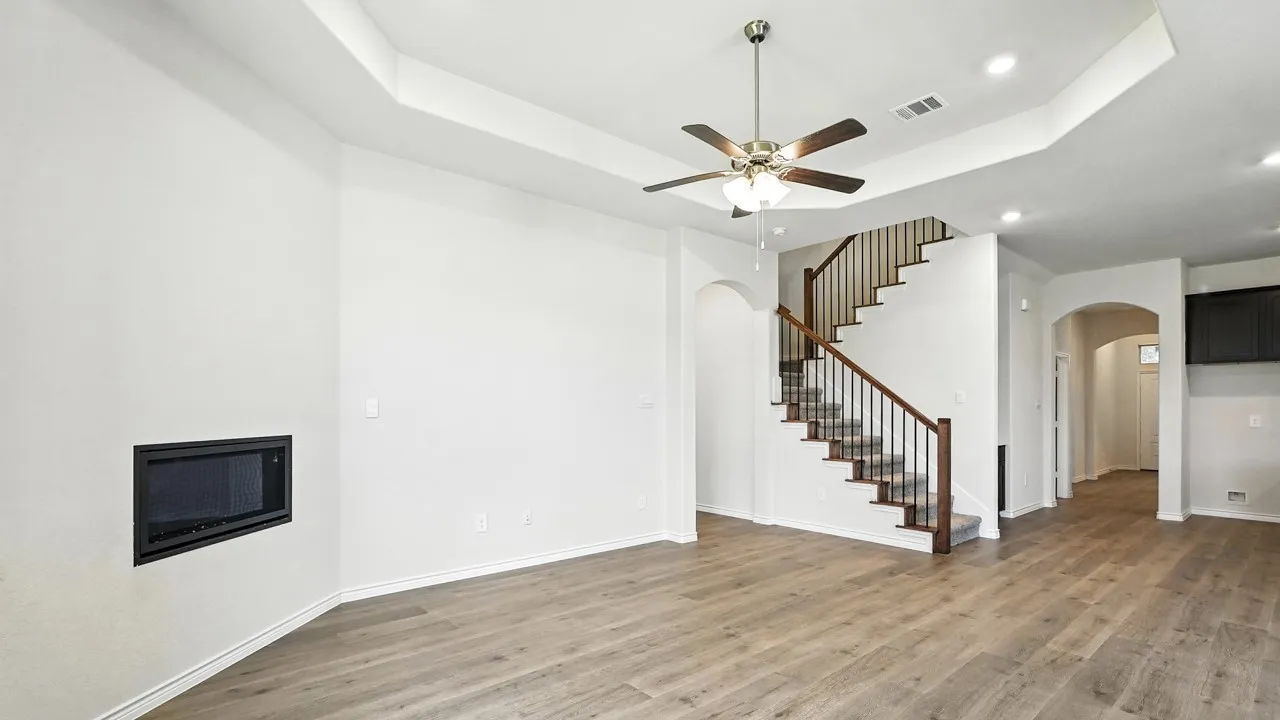 Unfurnished living room featuring arched walkways, light wood-type flooring, recessed lighting, ceiling fan, and a raised ceiling