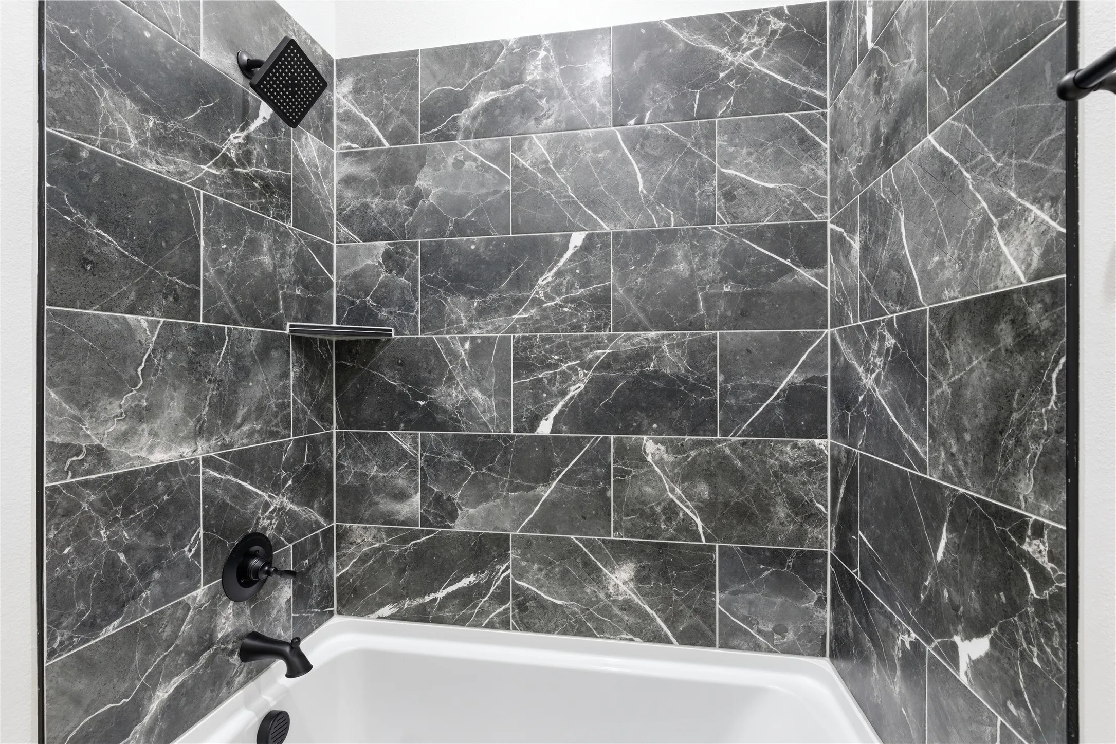Bathtub and shower combination featuring dark-toned, large format tile with white veining
